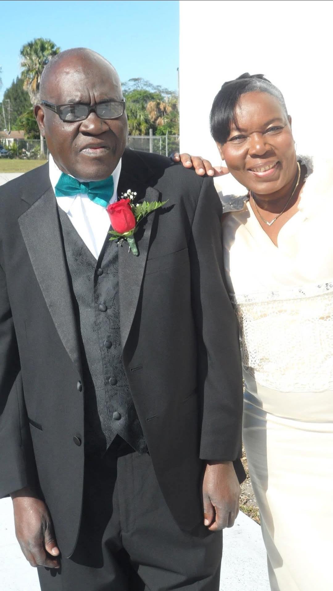 Couple in formal wear smiles outdoors on a sunny day, celebrating a special occasion.