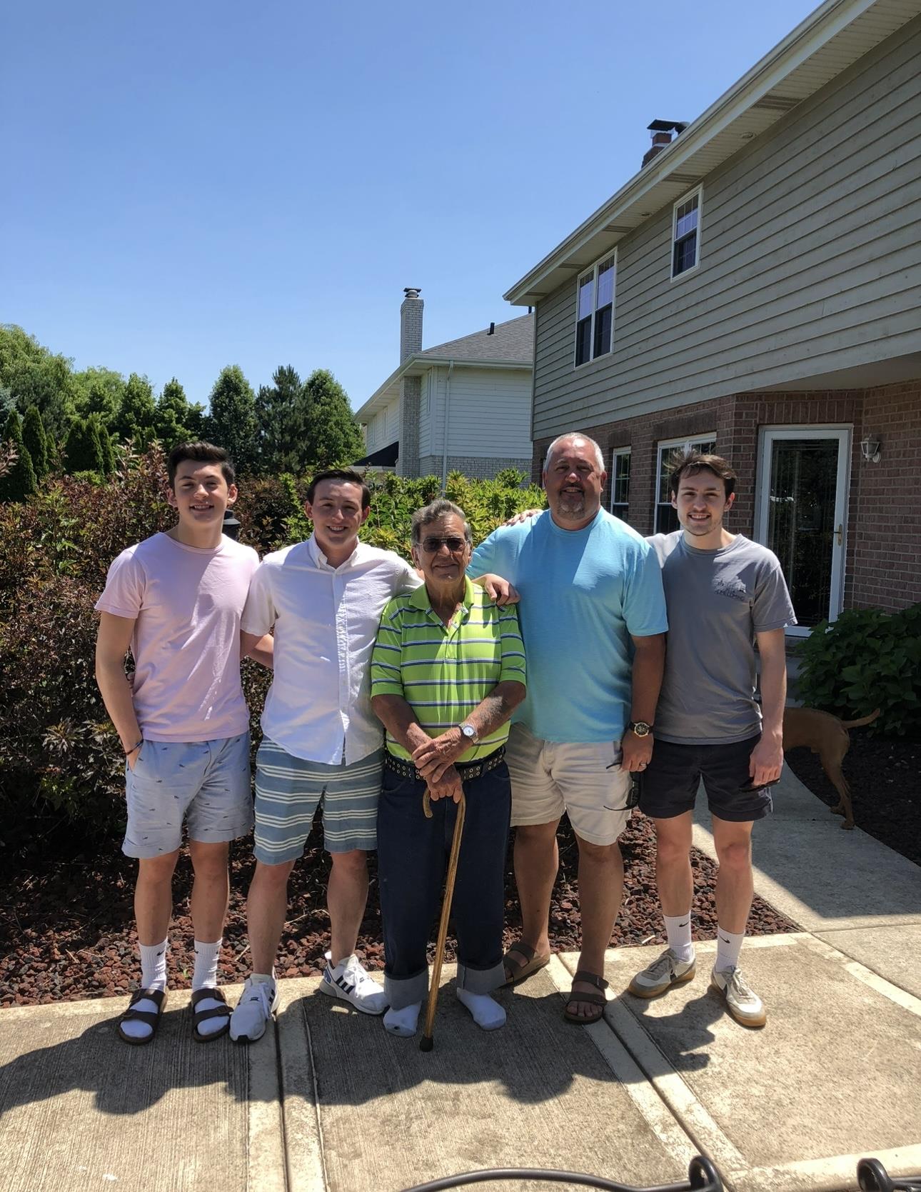 Family members gather in front of a house on a sunny day, sharing smiles and companionship.