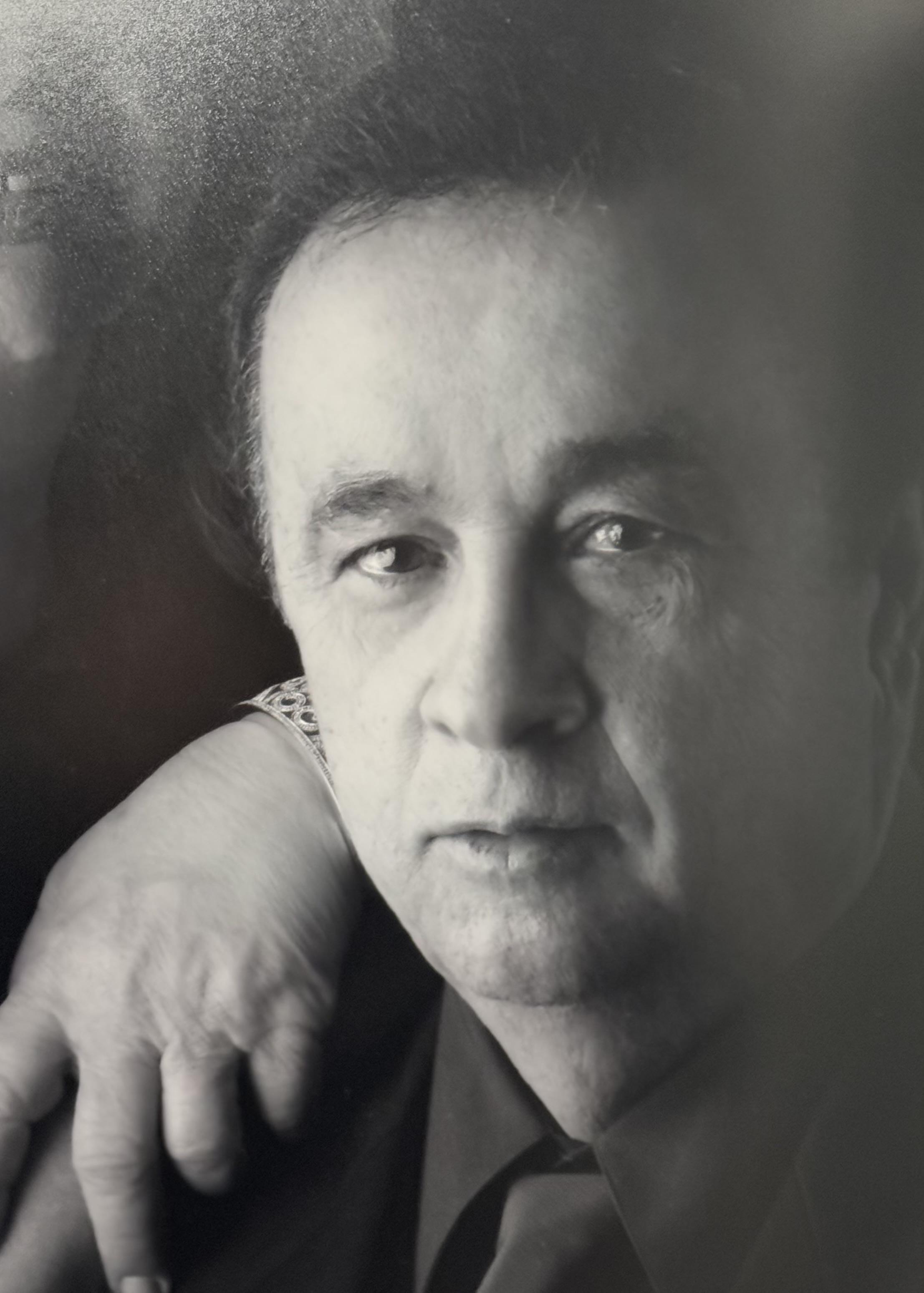 A man gazes intently while a hand gently rests on his shoulder, creating an intimate moment.