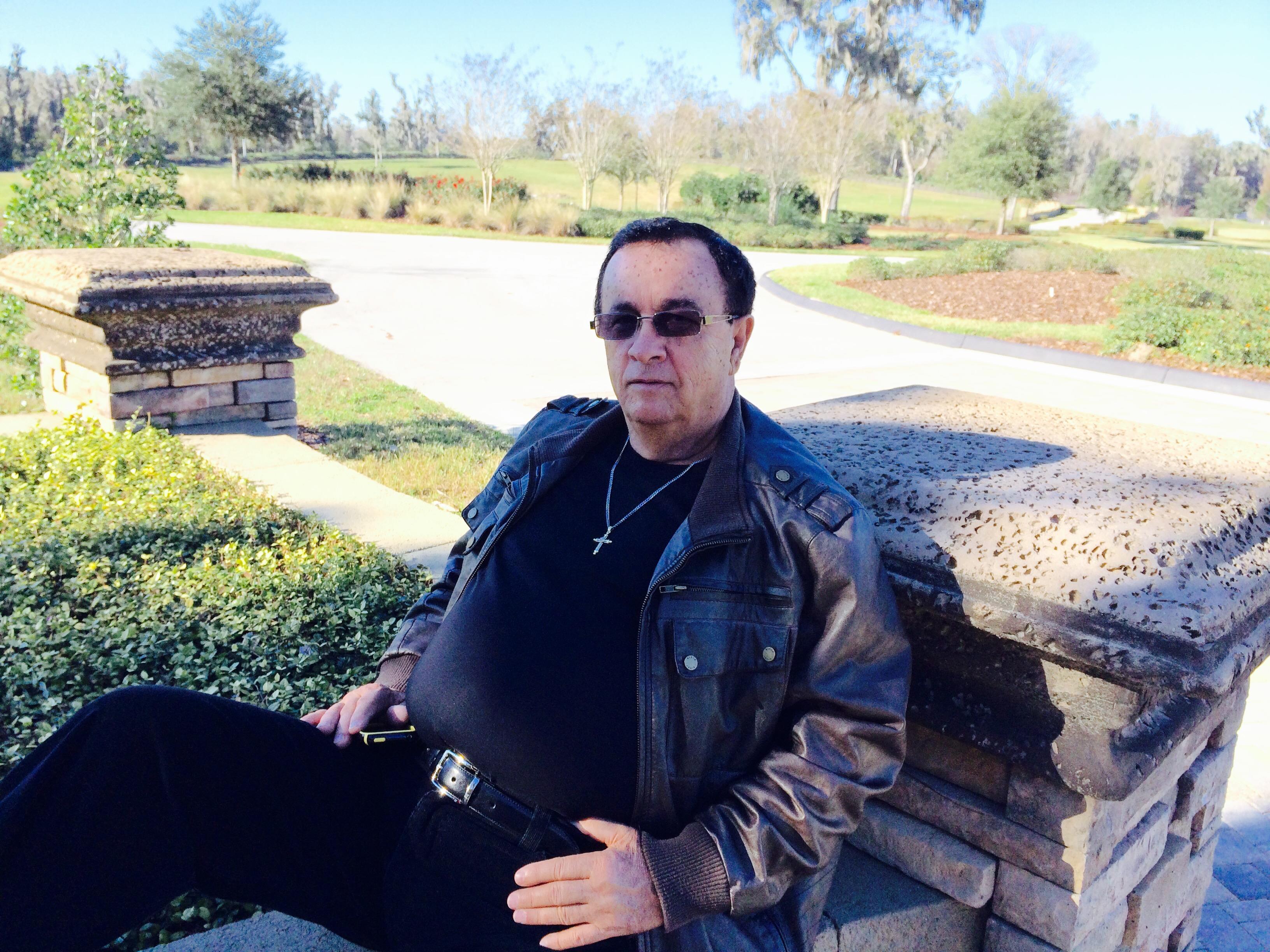 A man in black and gray relaxes on a stone wall, savoring the calm surroundings.