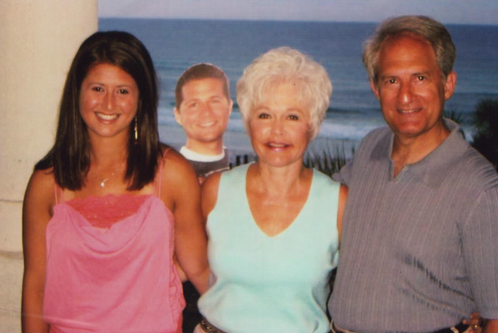 Three people stand together, smiling against a coastal backdrop with ocean waves at sunset.