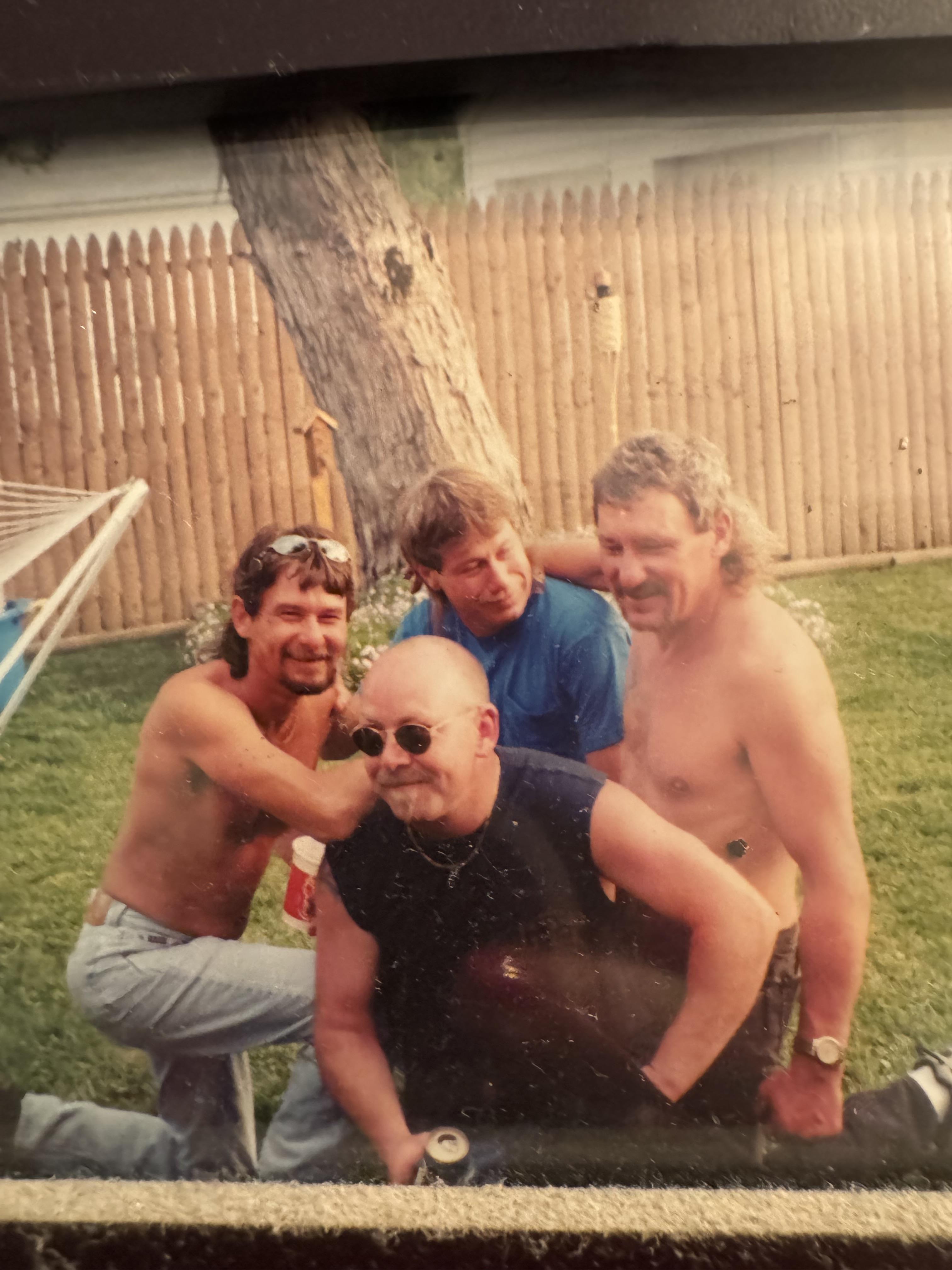 Four men share a lighthearted moment in a sunny backyard, showcasing friendship and fun.