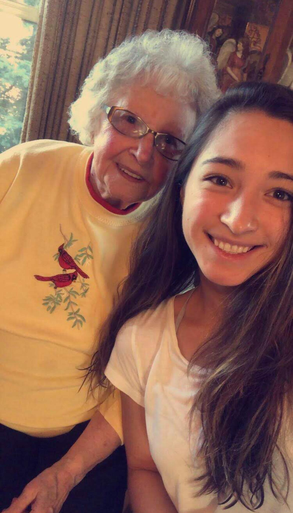 A young girl smiles widely alongside her grandmother, both sharing a special bonding moment indoors.