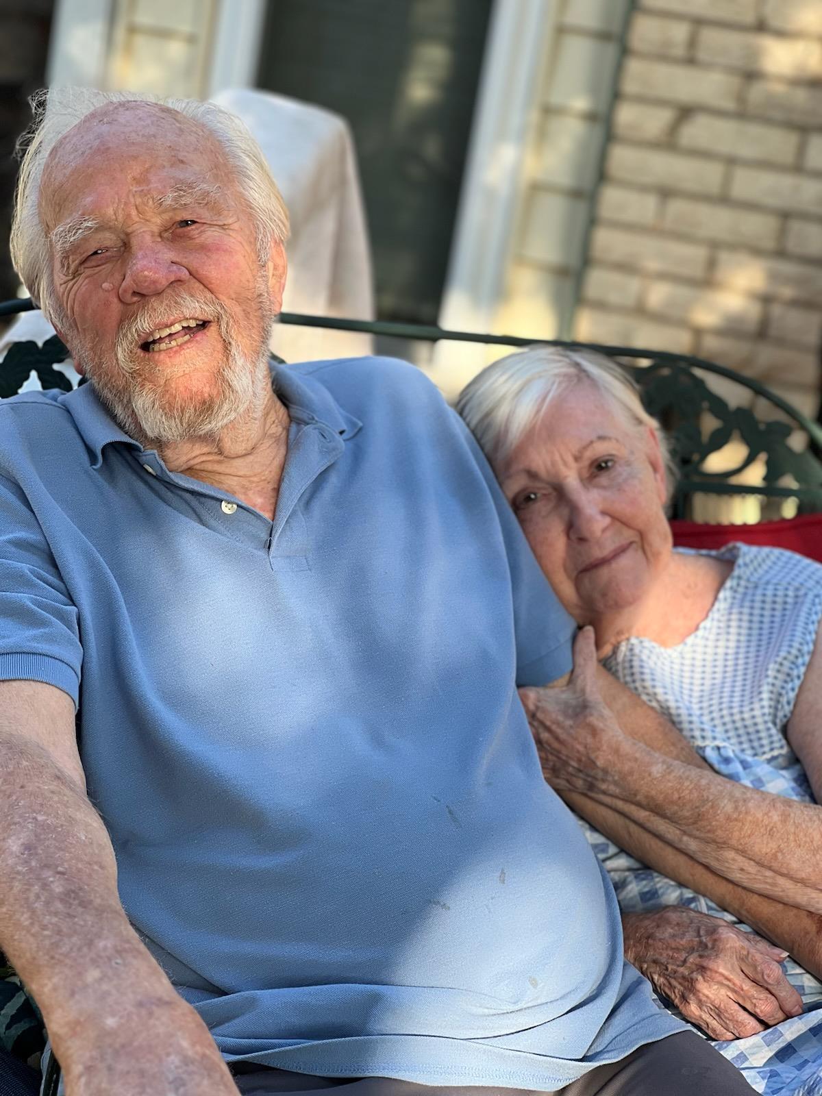 Two elderly individuals share a joyful moment while sitting outside and soaking up the sunlight.