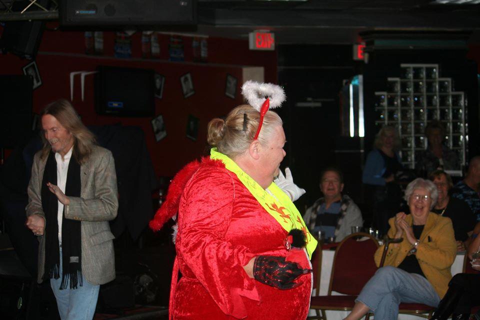 A vibrant performer in a red outfit engages the audience at a lively holiday gathering.