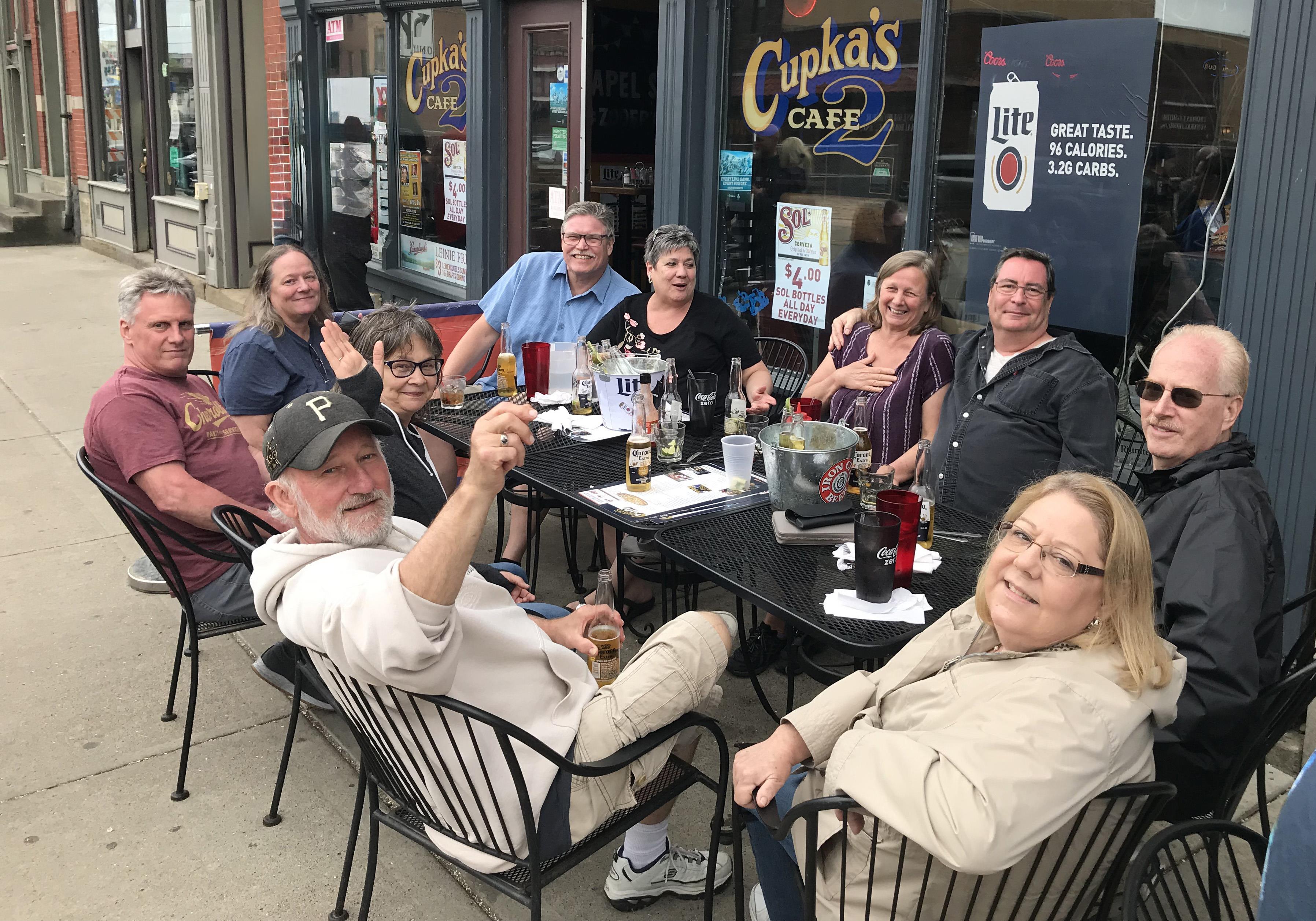People gather at a cafe terrace, sharing drinks and laughter on a pleasant day.