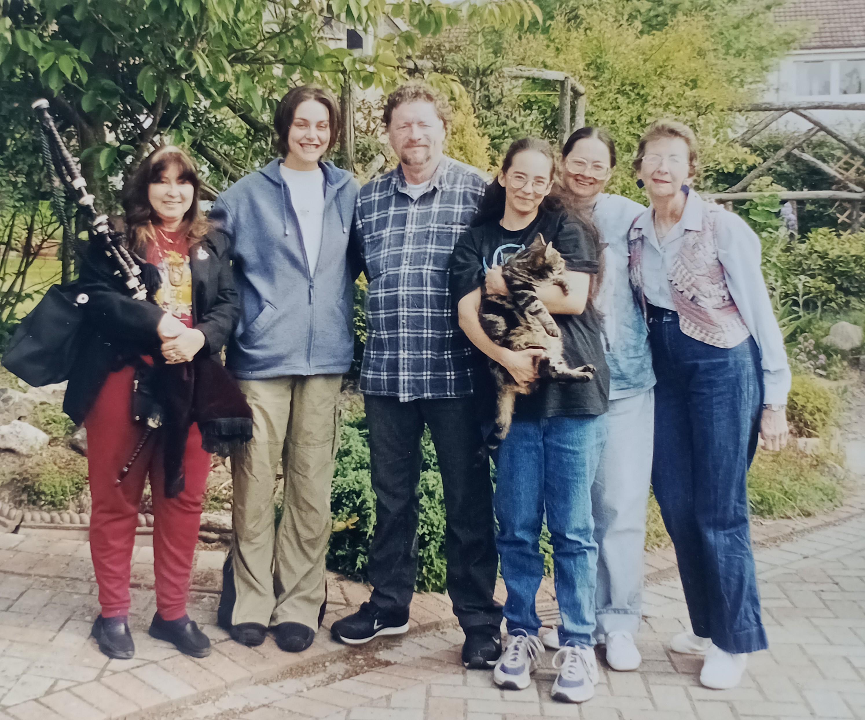 A group of six people smiles joyfully in a vibrant garden, each holding unique items.
