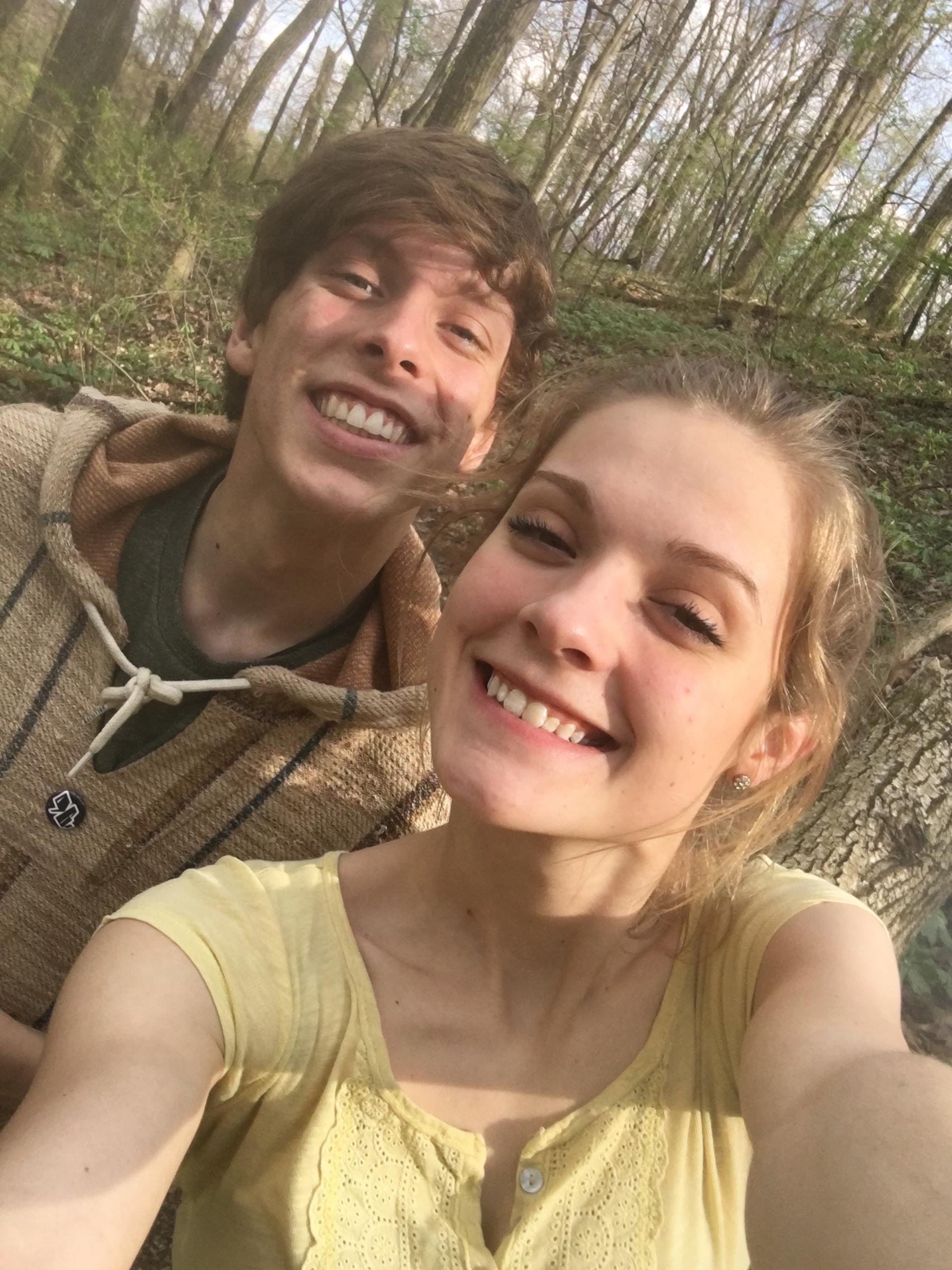Two friends share a cheerful selfie in a vibrant forest filled with greenery.