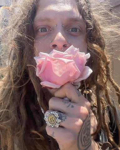 An individual showcasing a pink rose in a vibrant outdoor setting under sunlight.