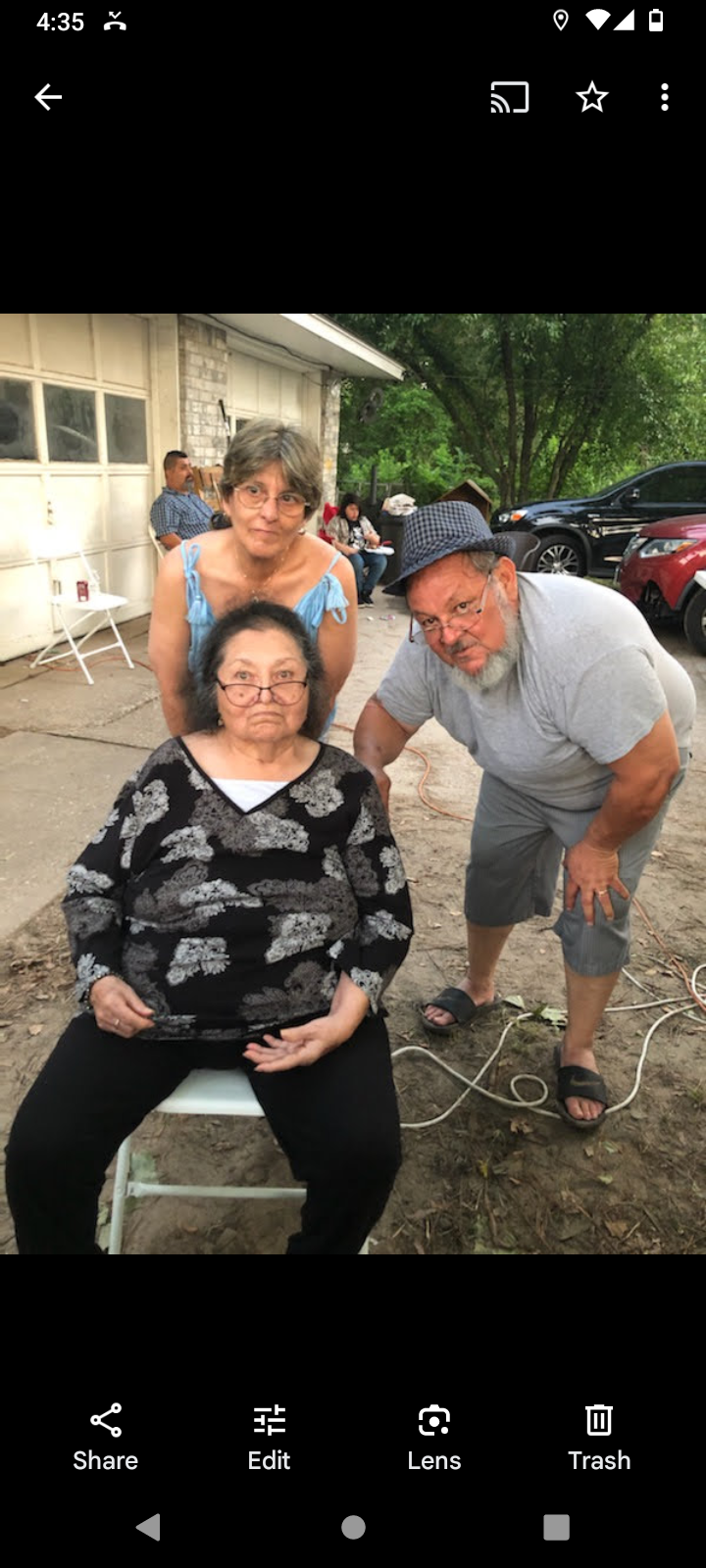 Three adults are enjoying a casual moment at a family gathering outside, sharing smiles.