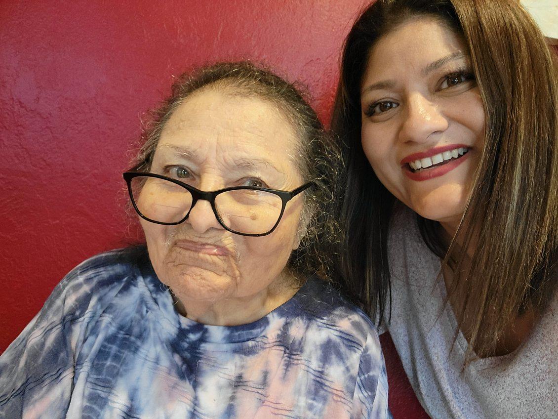 Two women smile happily at the camera while posing against a vibrant red backdrop.
