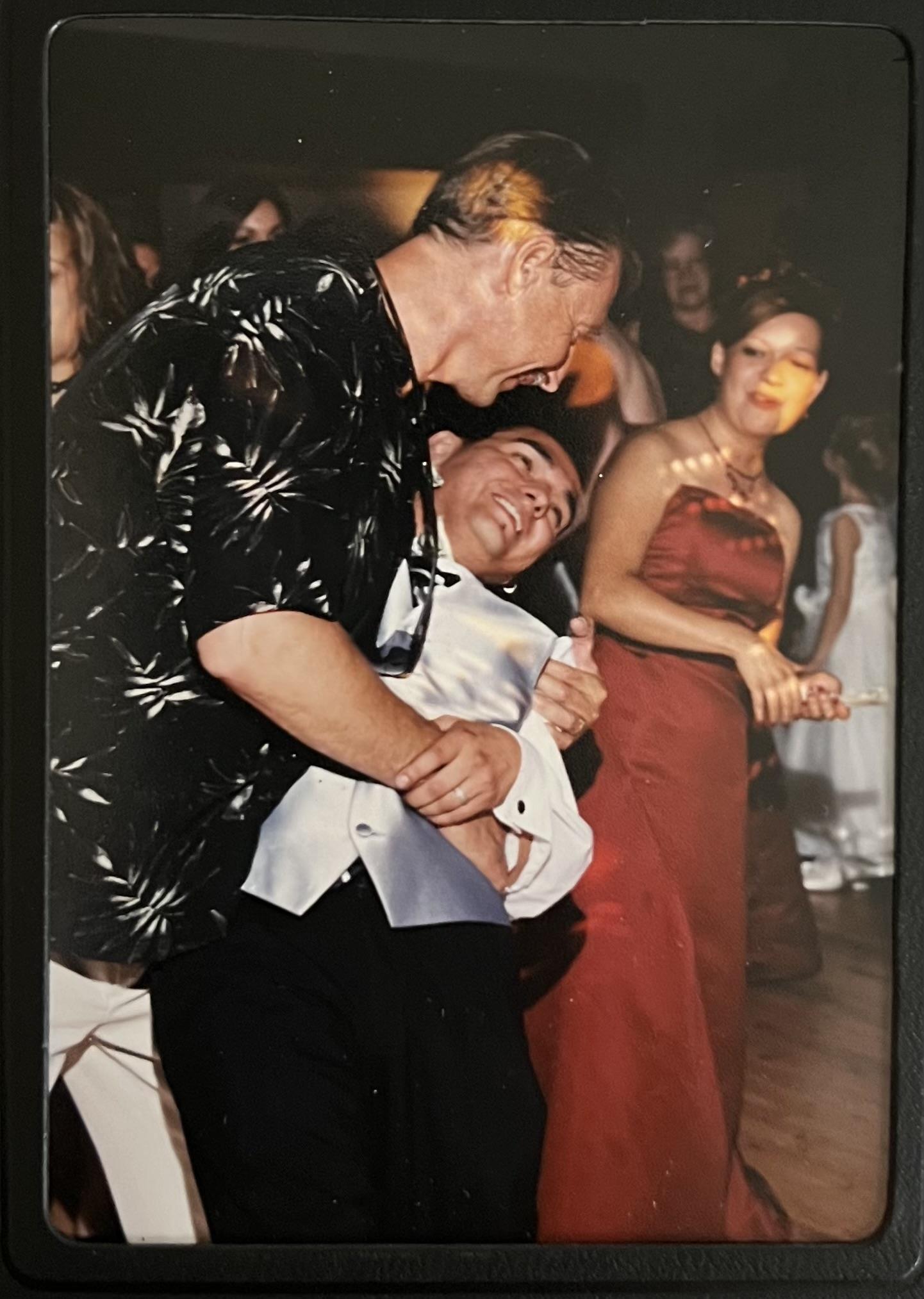 Two friends enjoy a playful moment while dancing at a lively celebration, surrounded by guests.