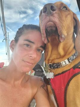 A person enjoys a cheerful moment with a large dog while capturing a selfie under the sun.