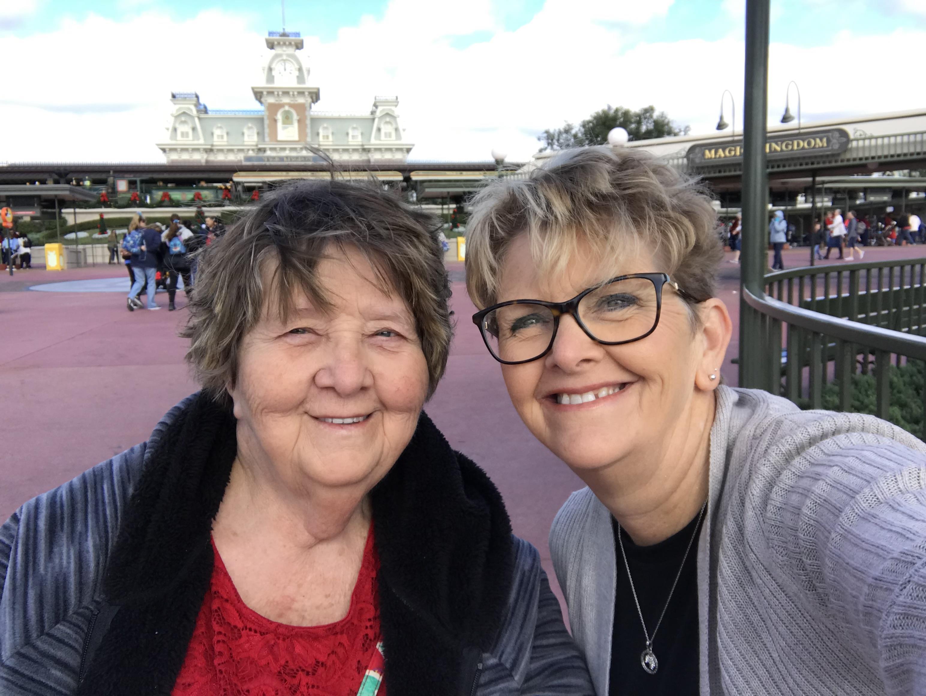 Two women smile happily together in front of an amusement park entrance during the cold season.