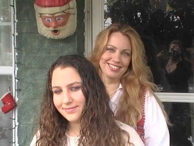 Two women smile for the camera in front of a home adorned with holiday decorations.