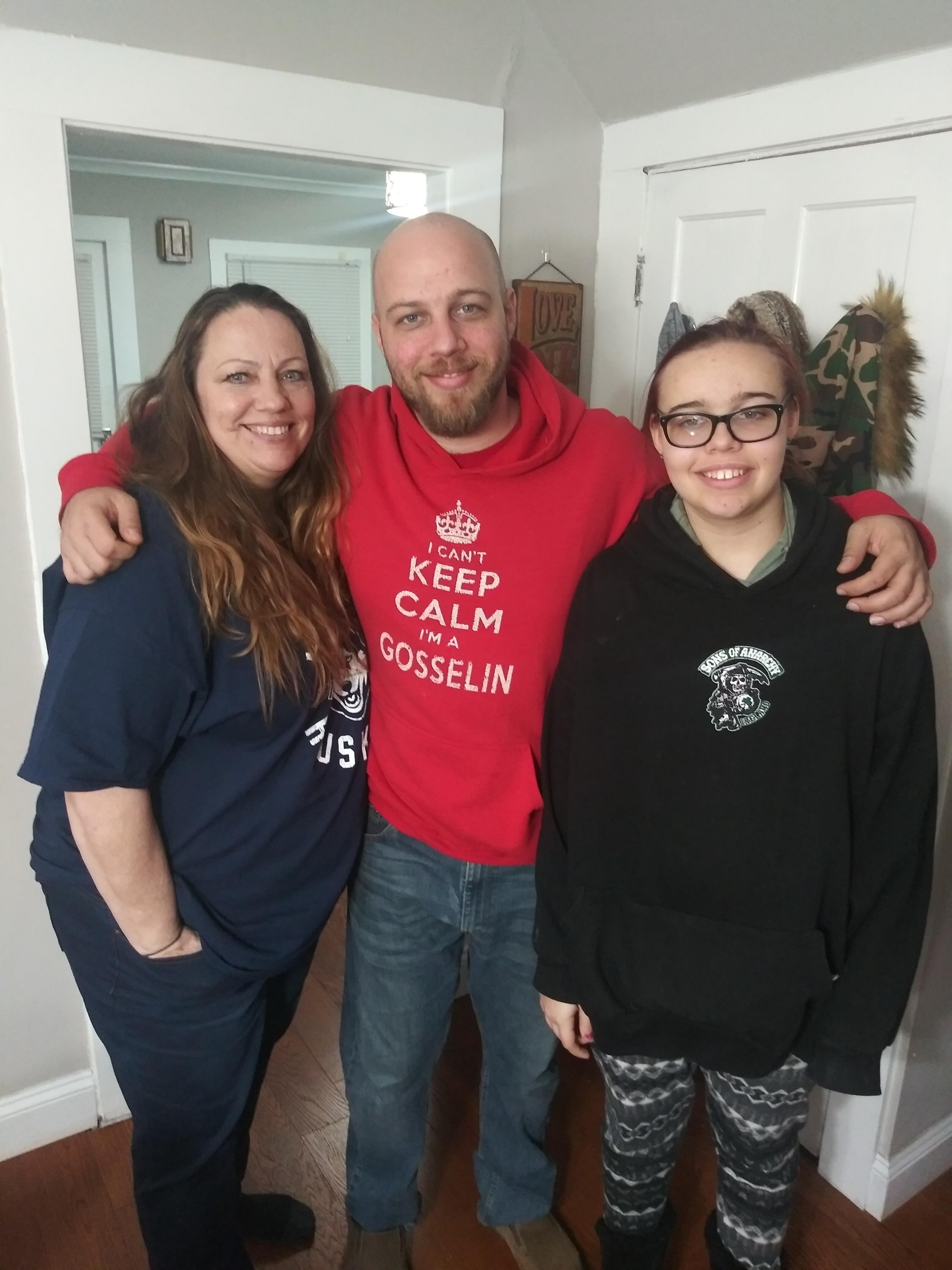Three family members smile warmly while posing together in a welcoming home environment.