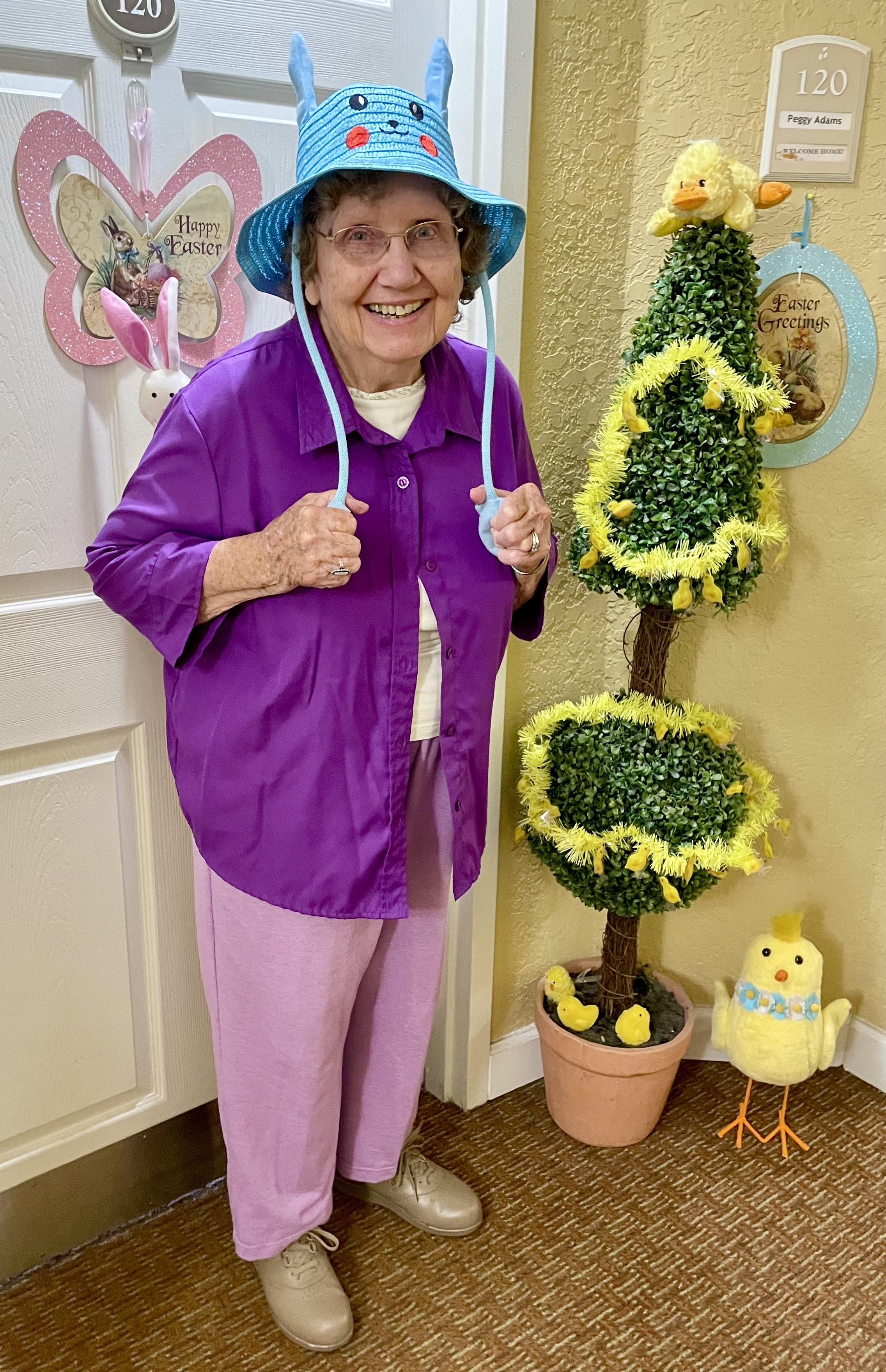 Joyful senior woman dressed in vibrant colors stands by festive Easter decorations.