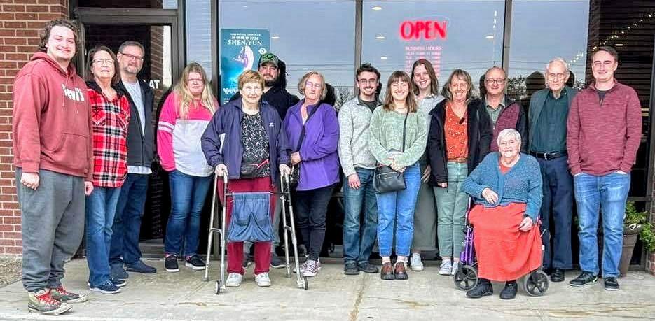 A large group stands outside a community center, smiling and enjoying their time together.