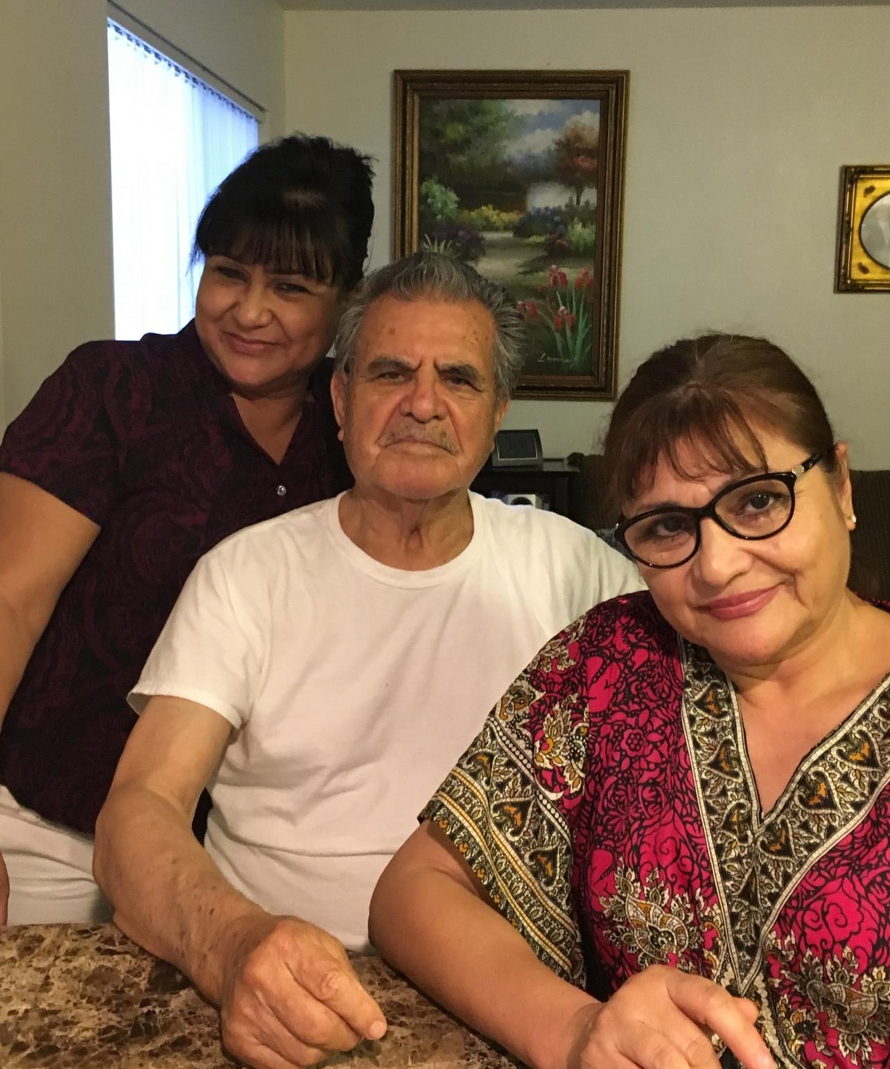 Three family members pose happily at a table in a warm and inviting living room.