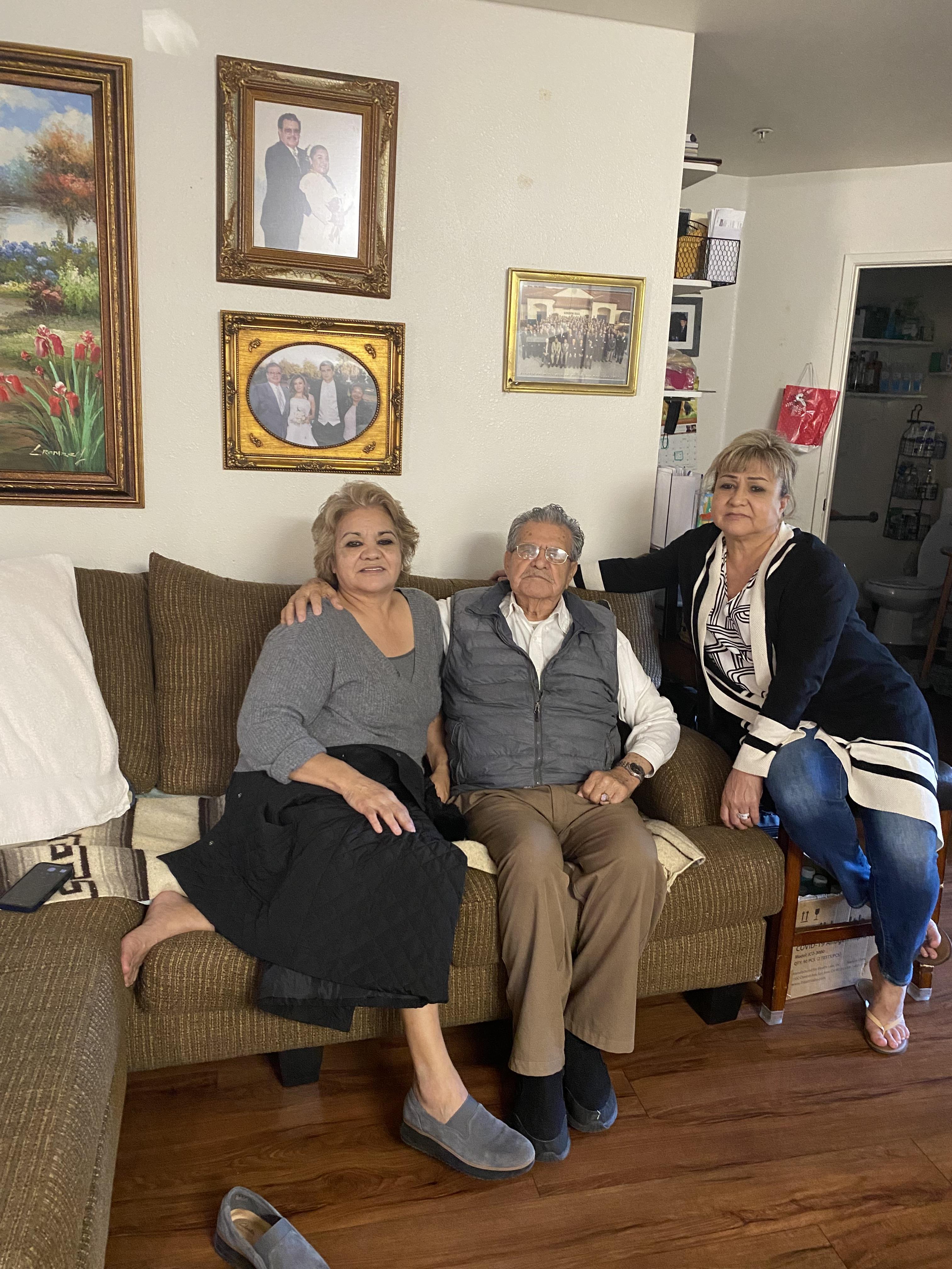 Three adults are seated together on a couch, enjoying a family moment in a warm living room.