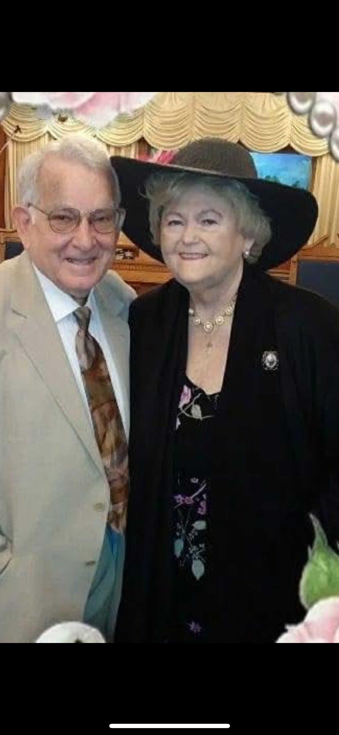 A joyful couple dressed in formal attire stands close, sharing a warm moment at an event.