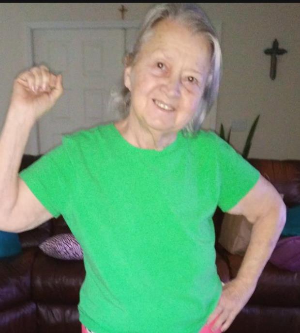 An elderly woman in a bright green shirt is joyfully smiling and dancing.