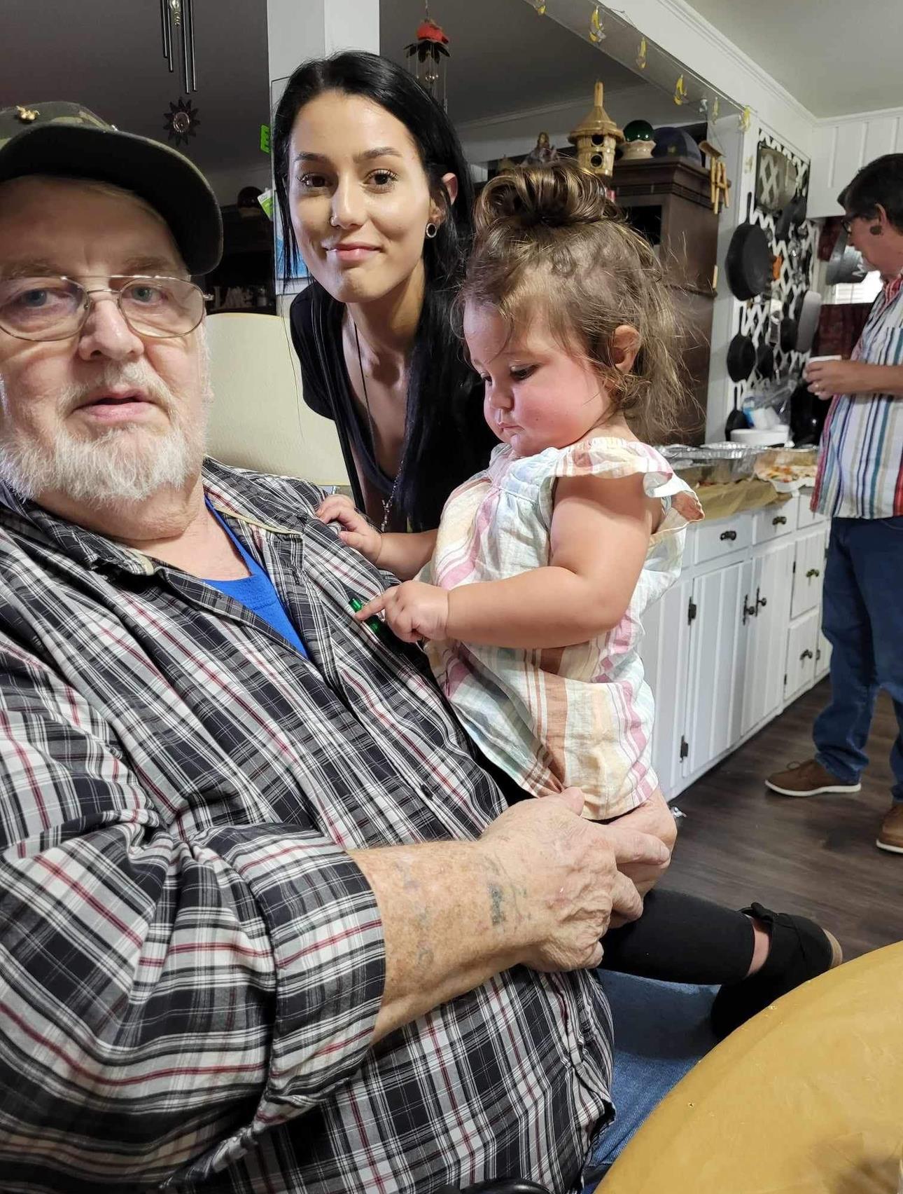 A warm moment as a grandfather cuddles his granddaughter while her mother smiles beside them.