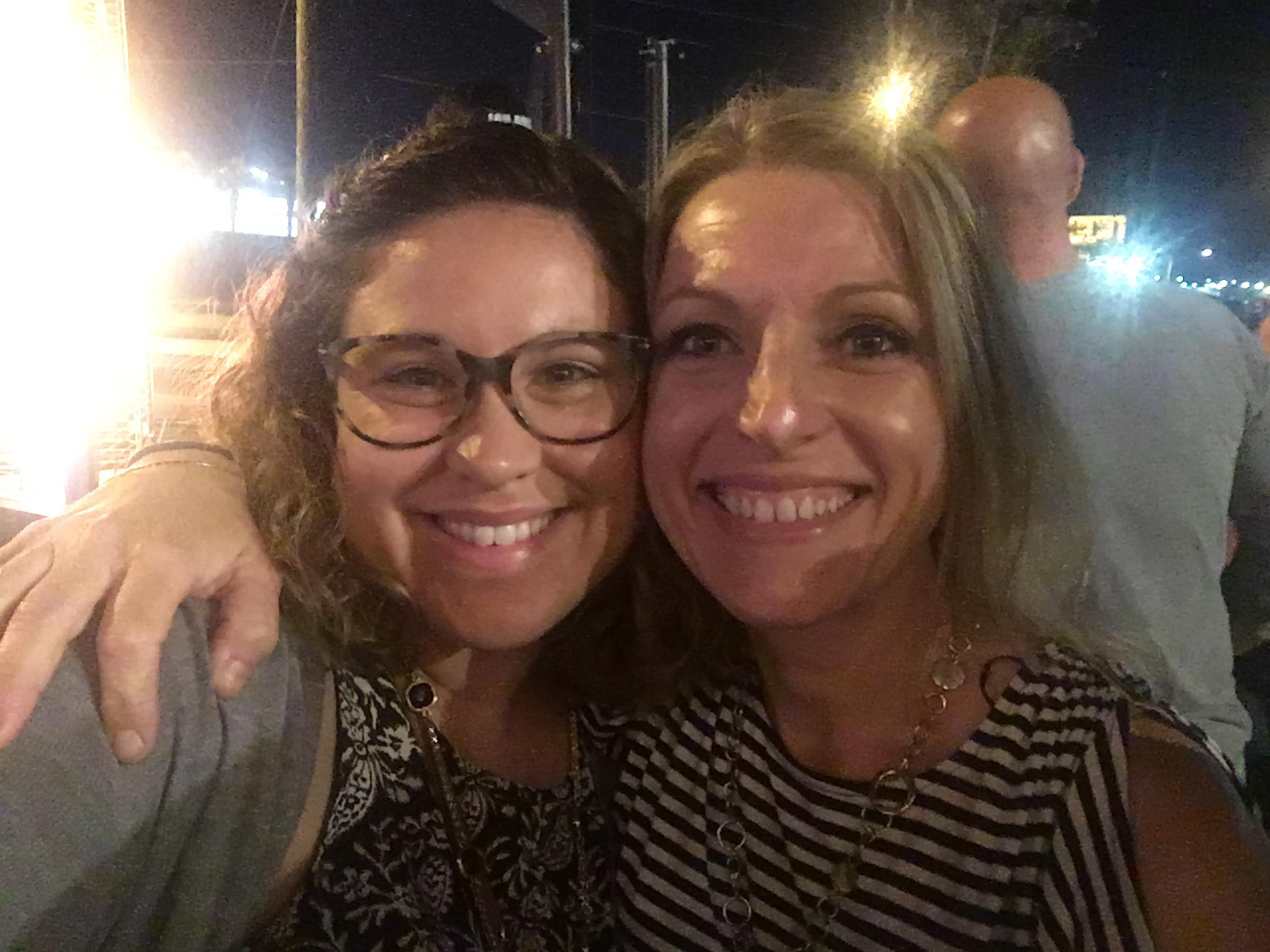 Two friends smile happily for a picture during a lively summer festival at night.