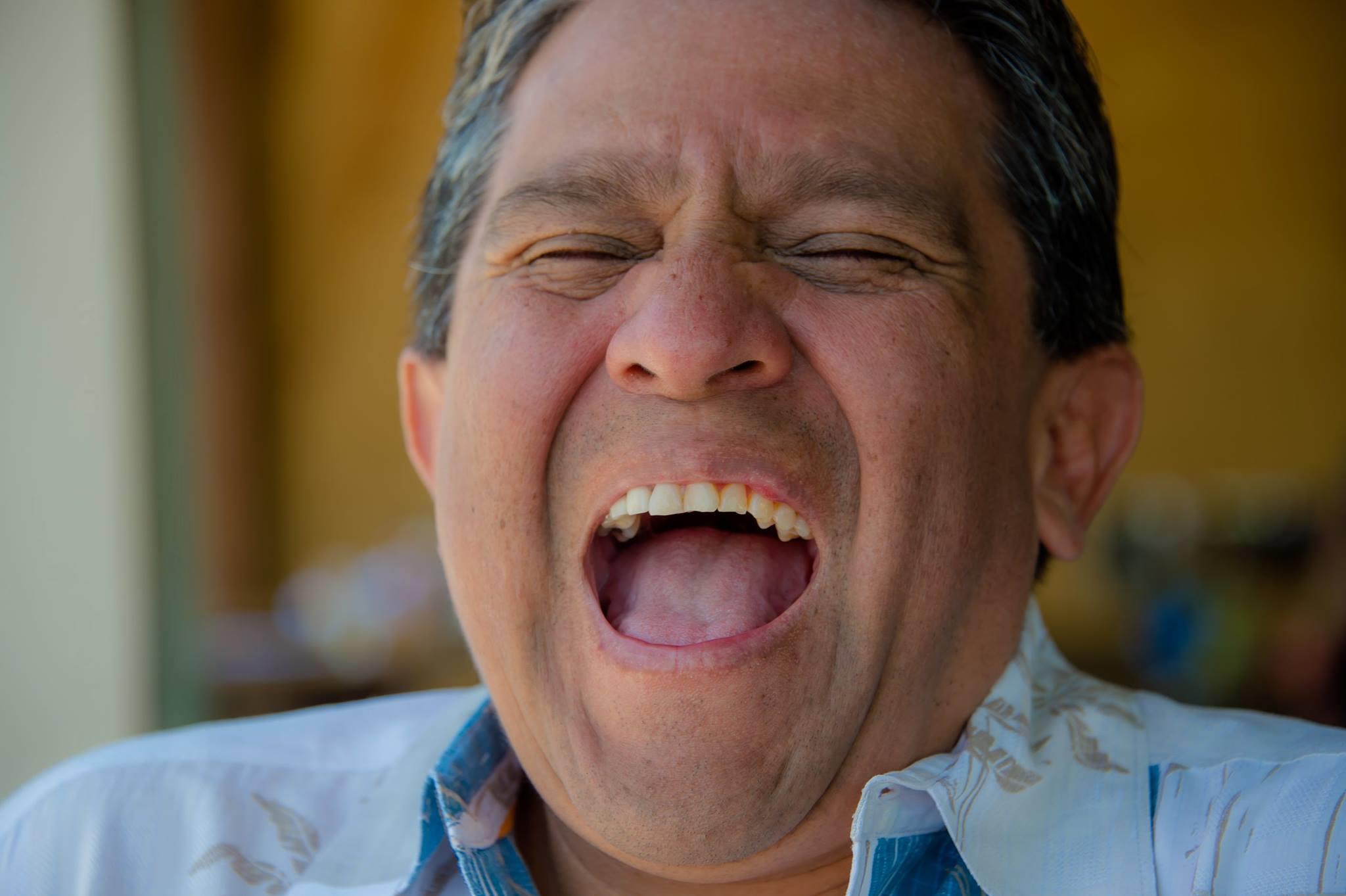 A man is laughing heartily, capturing the joy of friendship and sunshine during a social gathering.