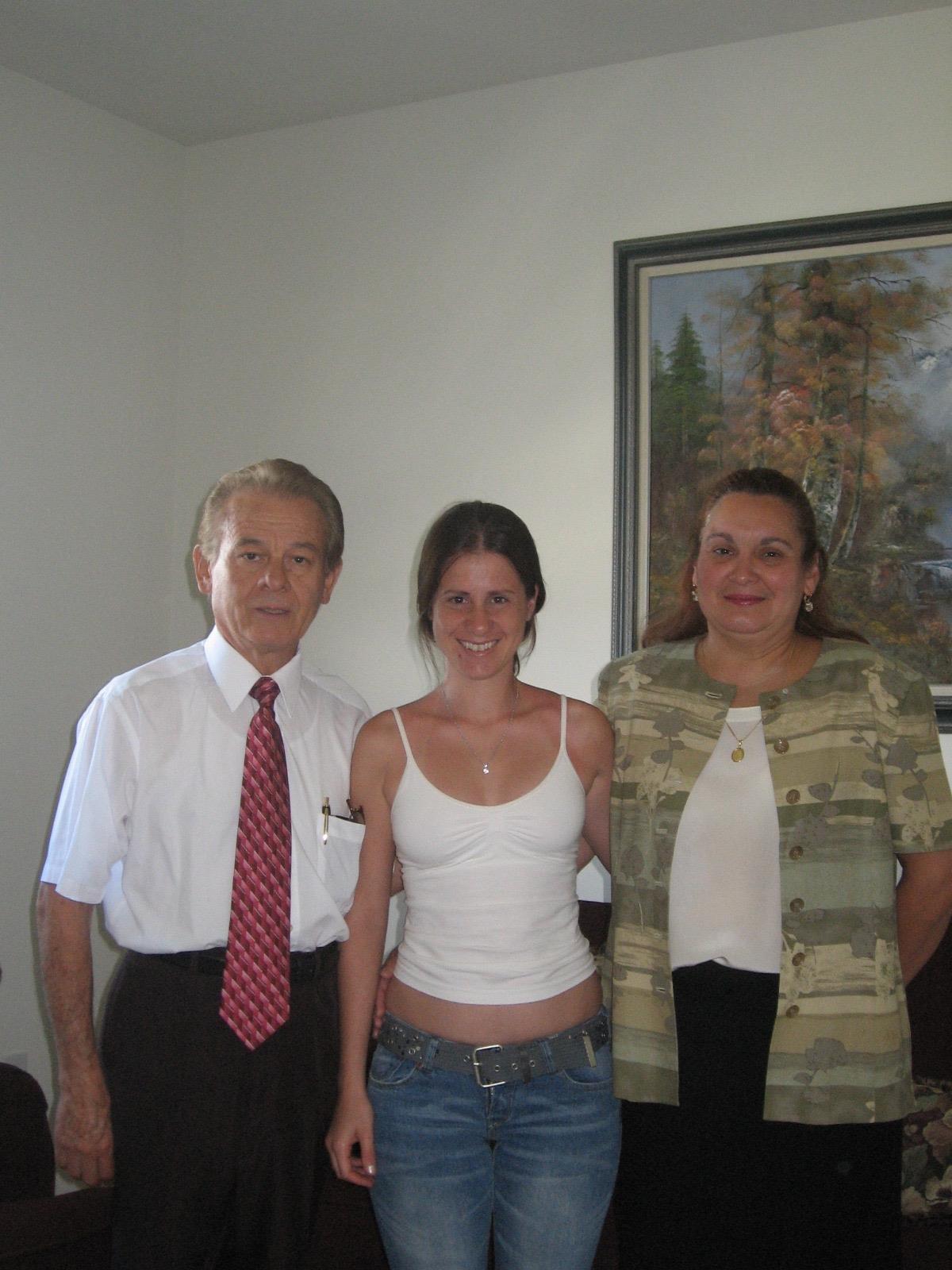 Three people stand together in a bright living room, smiling and posing for a photo.