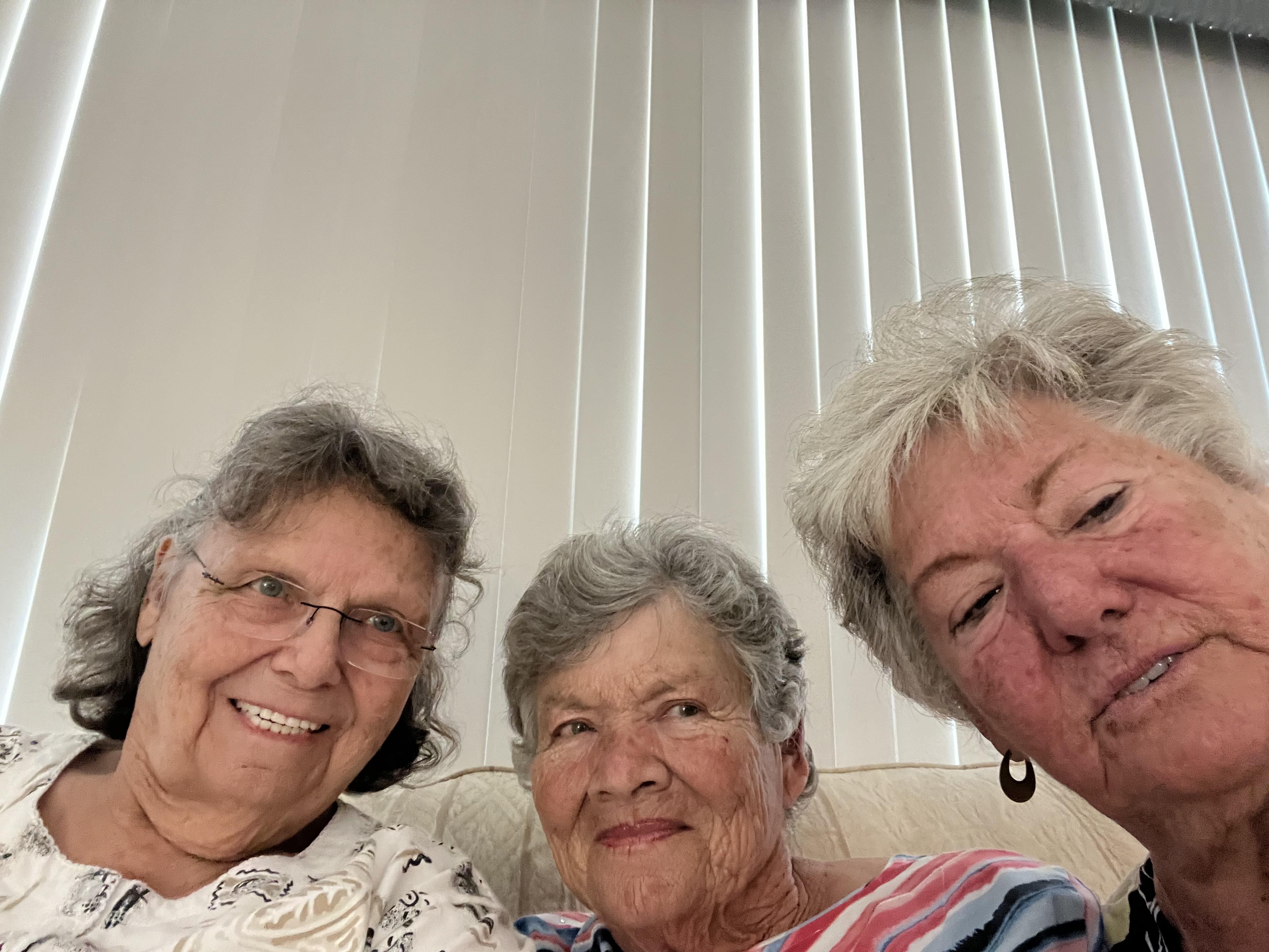 Three happy elder women share smiles and laughter during a joyful gathering in their living room.