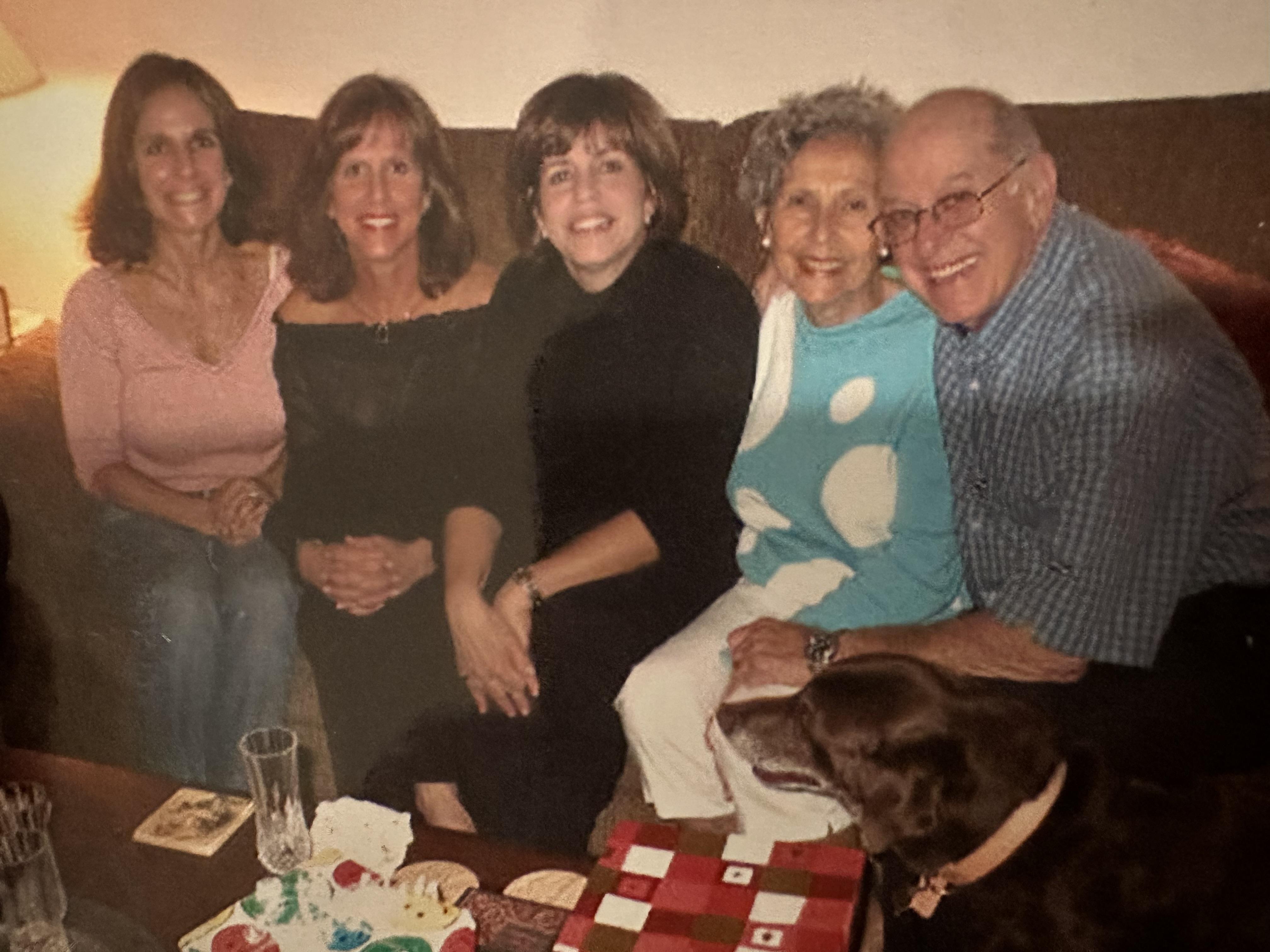 Friends and family sharing laughter and joy in a warm living room with snacks and a dog nearby.