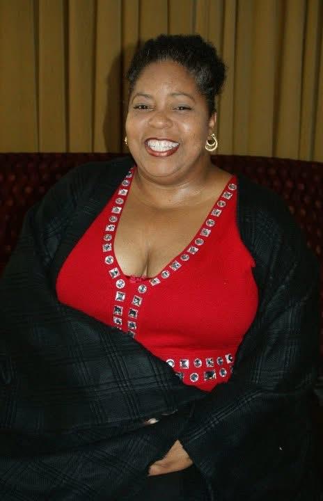 Woman beams joyfully while wearing a stylish red outfit with decorative elements and a secure wrap.