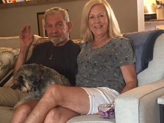 Couple enjoys their time together on a couch while their dog relaxes in their lap.