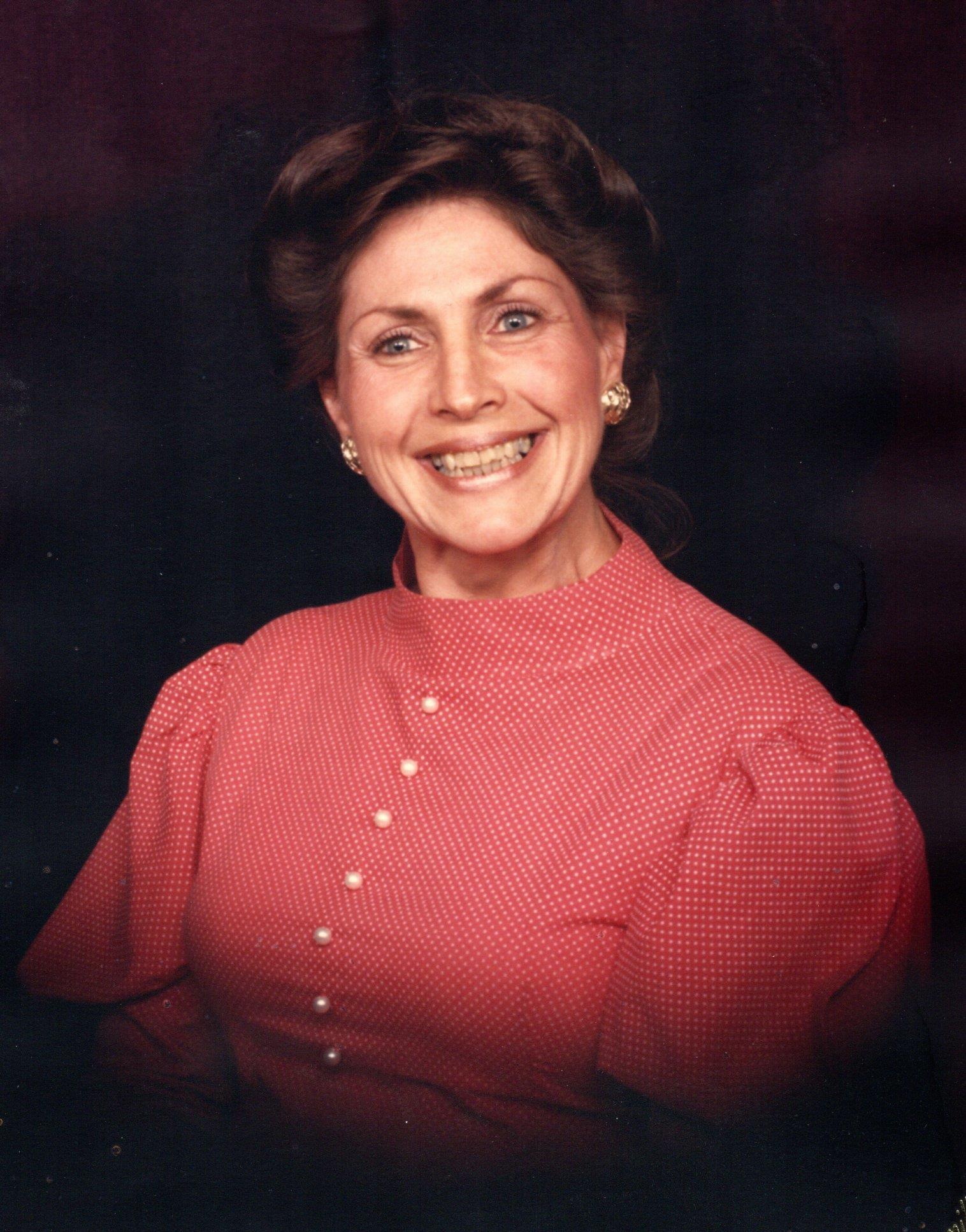 A woman in a pink blouse with a warm smile shows off her classic hairstyle against dark.