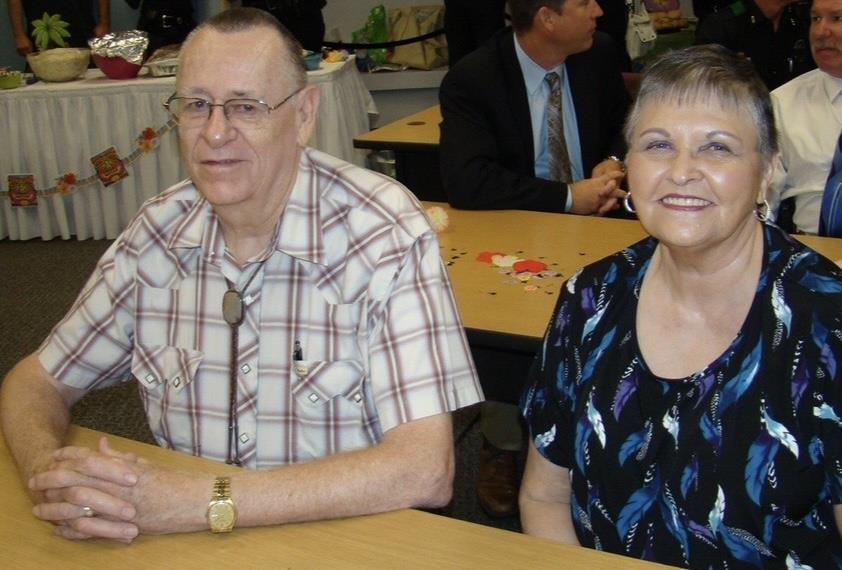 An older couple smiles together at a community event, surrounded by friends and decor.