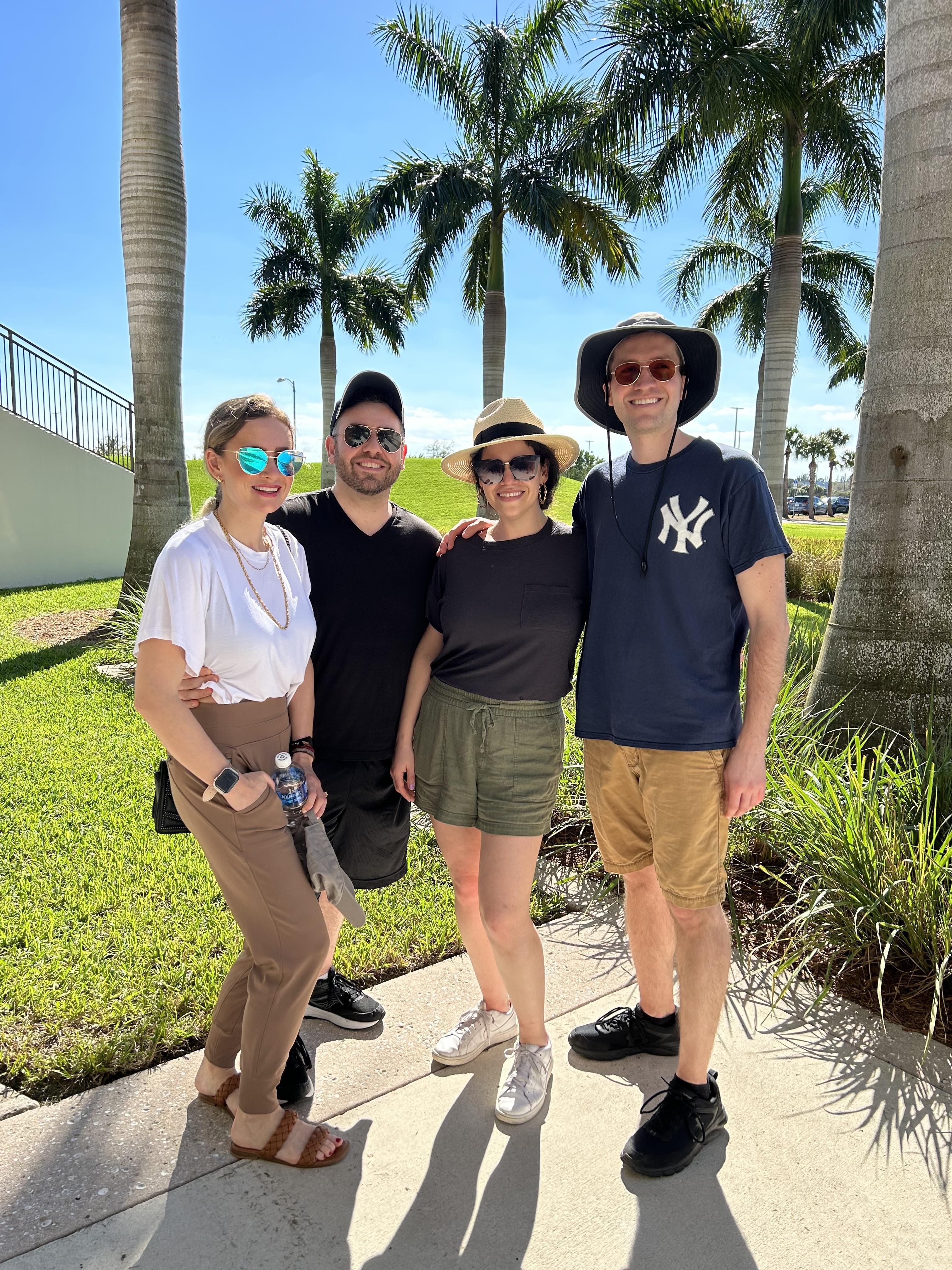 Group of four friends poses happily under palm trees during a sunny day together.