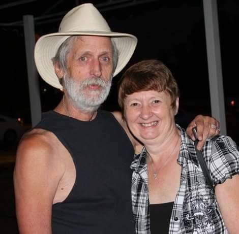 A couple poses happily for a picture, enjoying their time at a social event outside in summer.