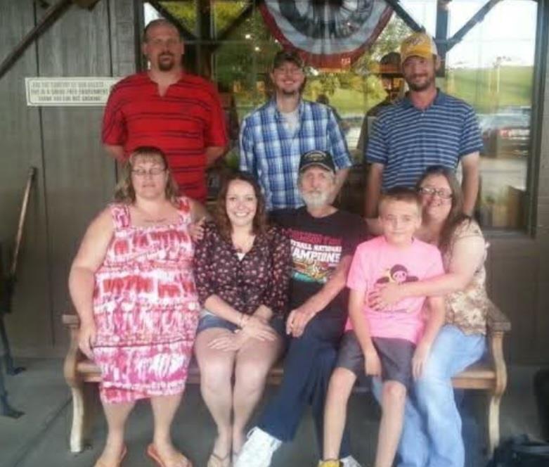 A joyful family reunion takes place outside a rustic venue with smiles and casual clothing.