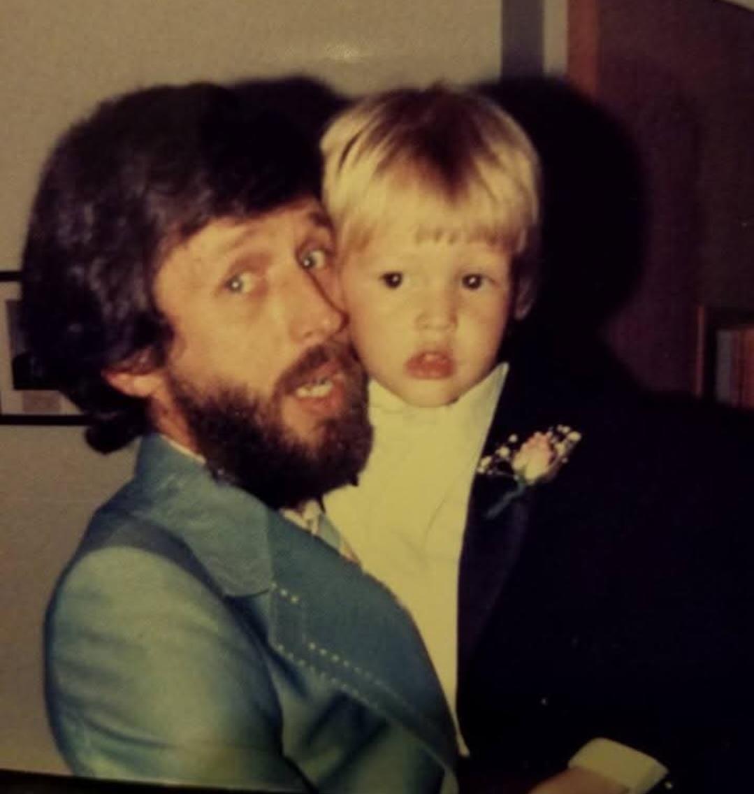 A father holds his young son close while attending a special event, both dressed in formal attire.