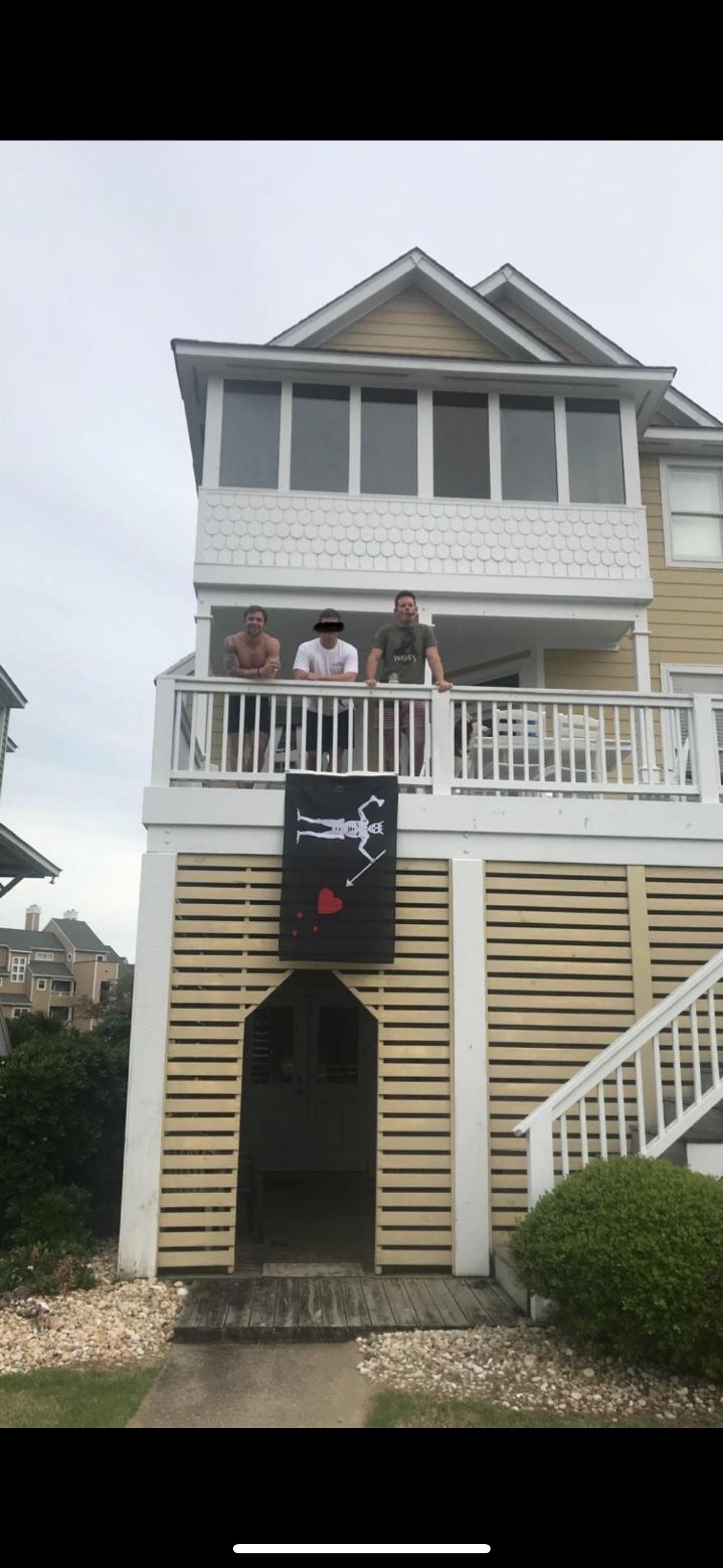 A group of individuals stands on a balcony showcasing a unique banner with a playful theme.