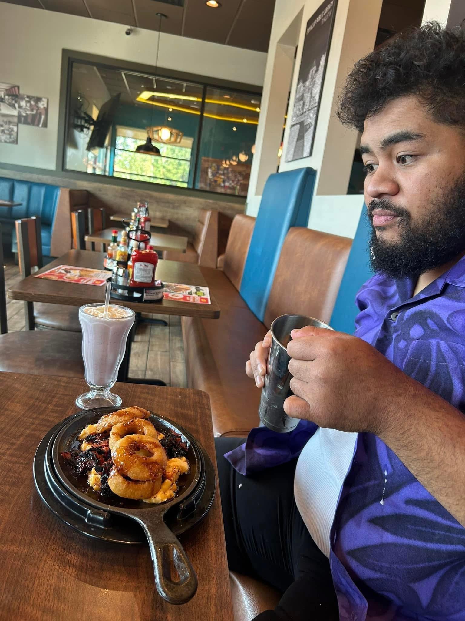 A young man sits at a restaurant table, savoring a dessert while sipping a drink.