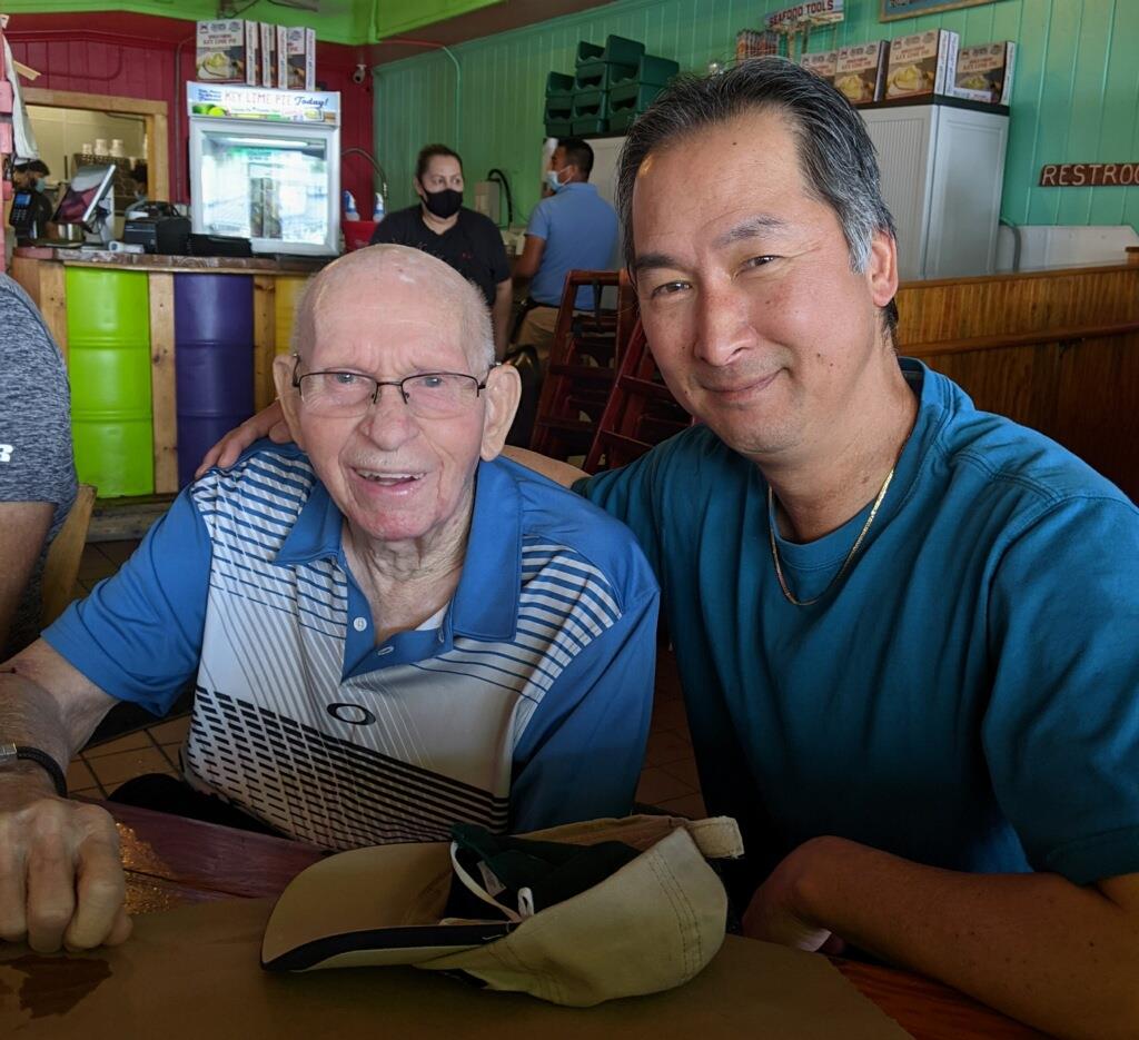 Two men share a warm moment at a restaurant, with smiles and a relaxed atmosphere around them.