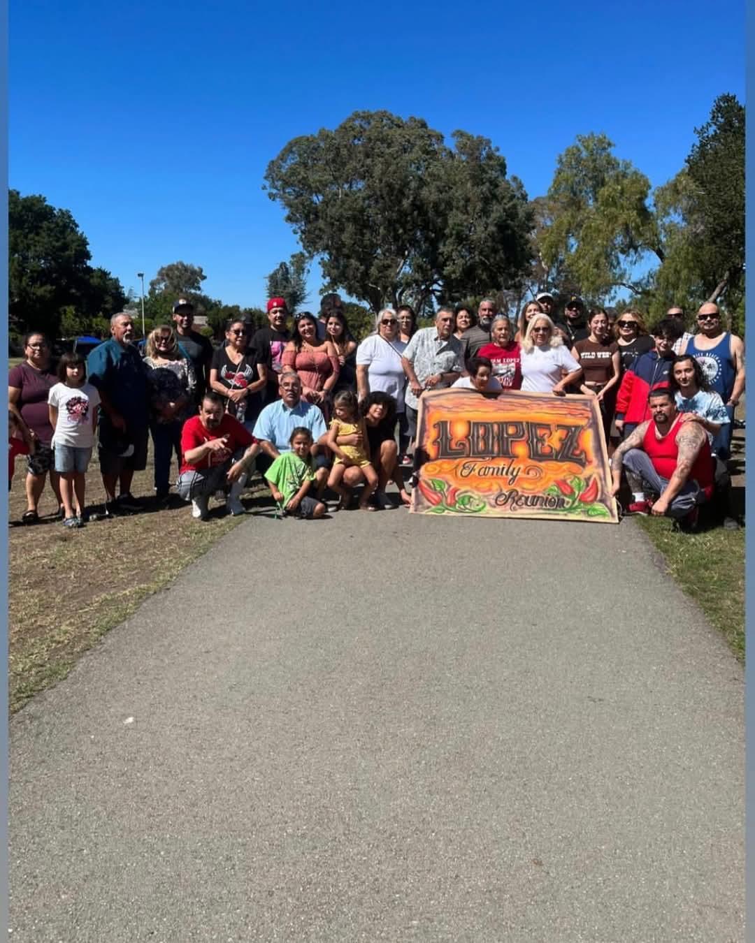 Large group of family members smiling and posing together at a park during a reunion event.