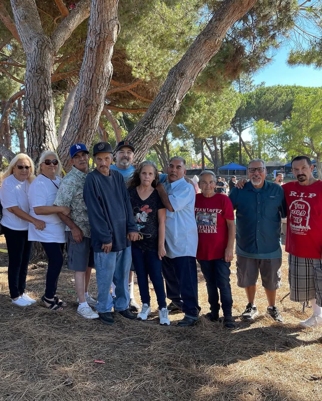 Group of friends and family pose together, enjoying a sunny day at the park, surrounded by trees.