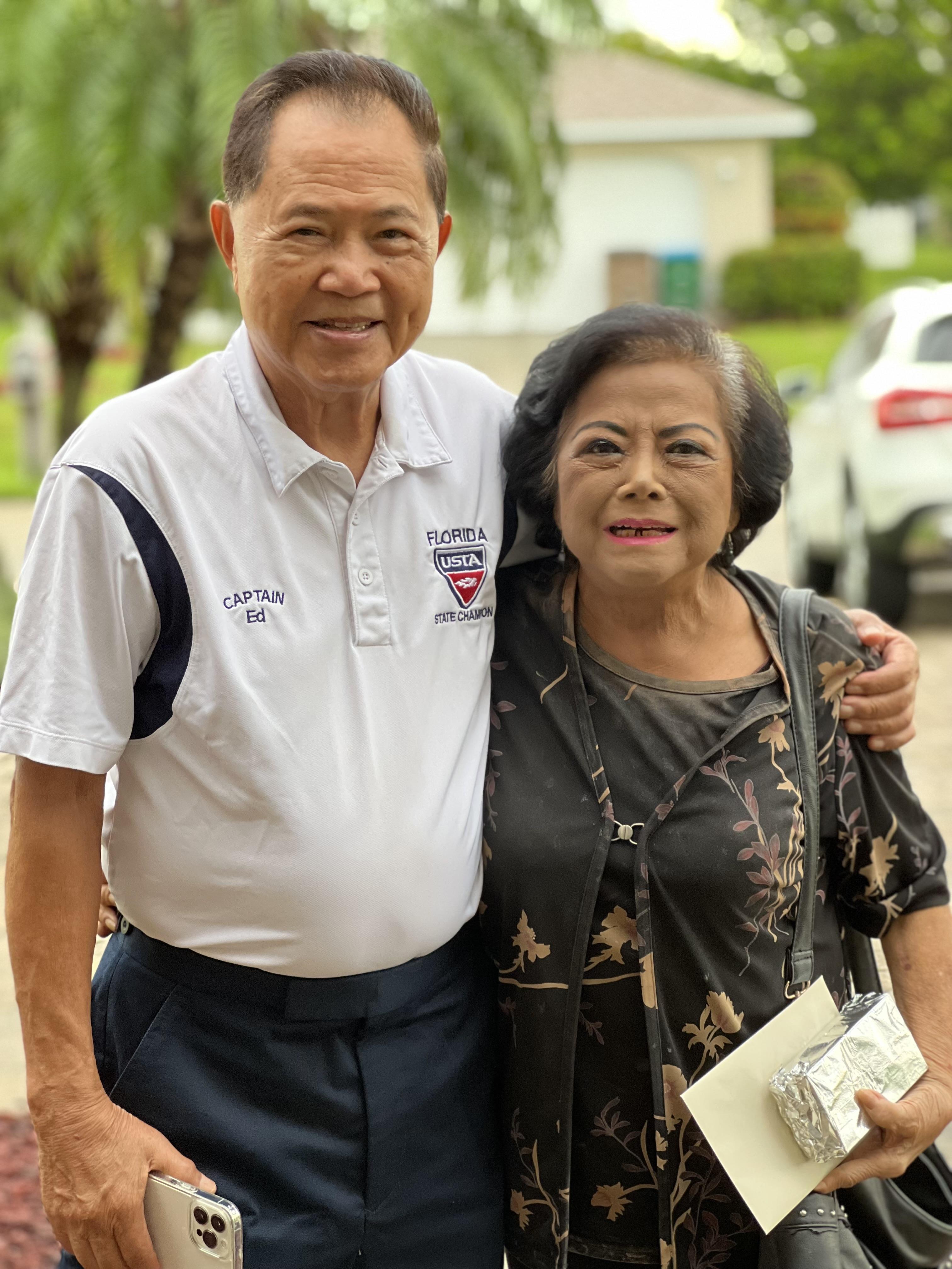 Two friends smile warmly while embracing outside a home on a bright Florida day.