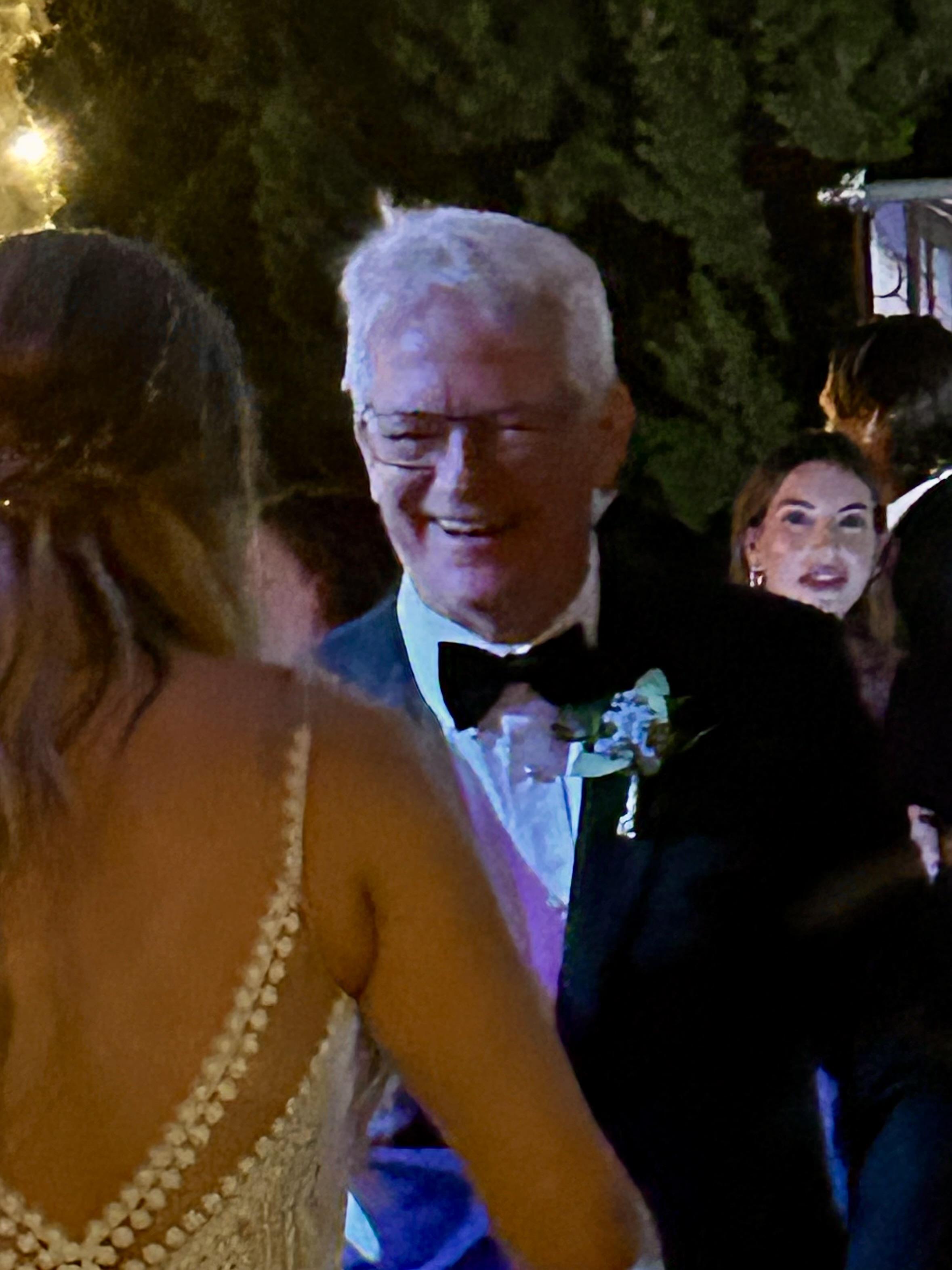 A man in a tuxedo smiles and engages with a woman in a beautiful dress at a festive gathering.
