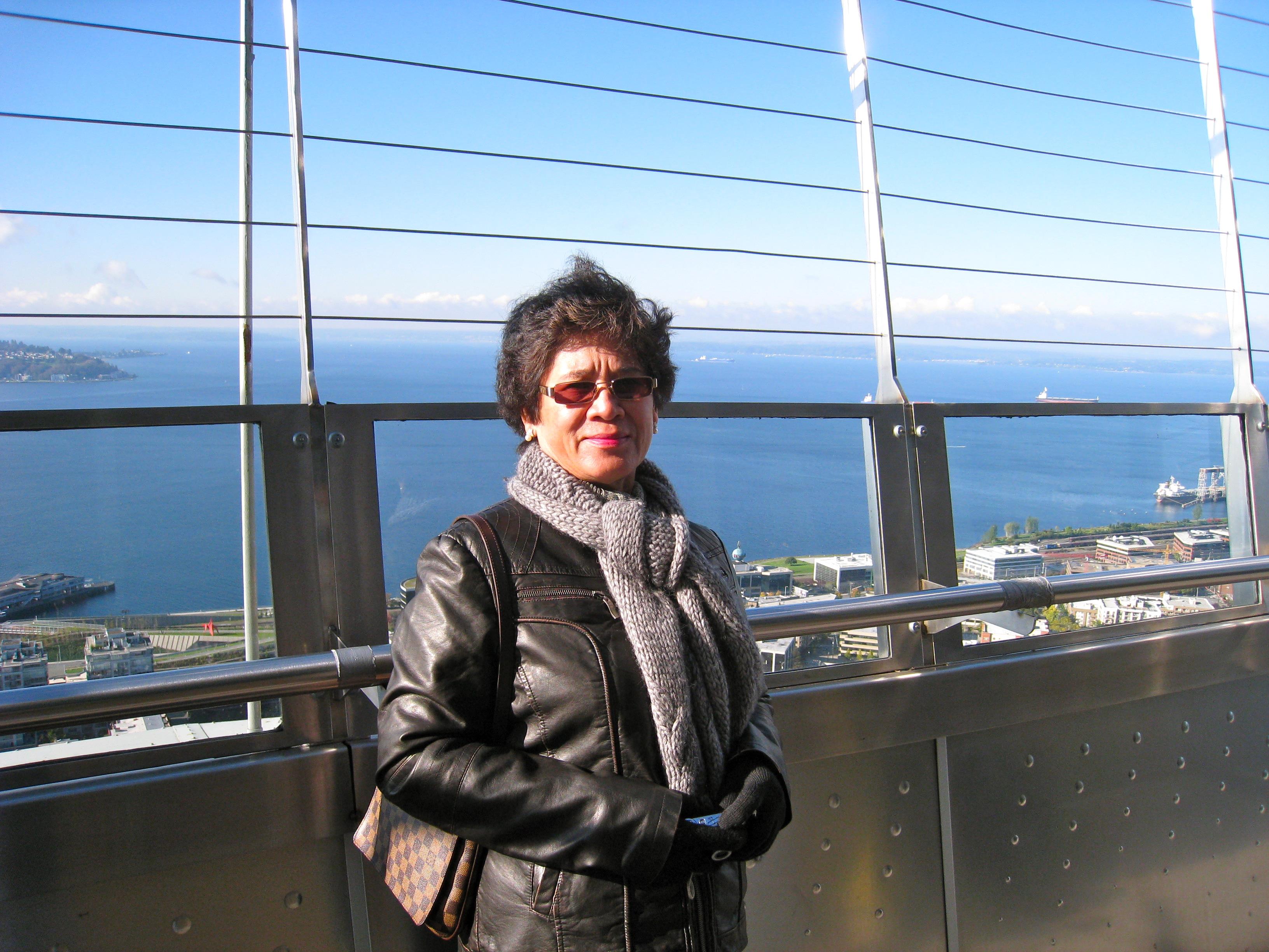 A woman stands confidently at an observation deck, admiring the ocean view and distant coastlines.