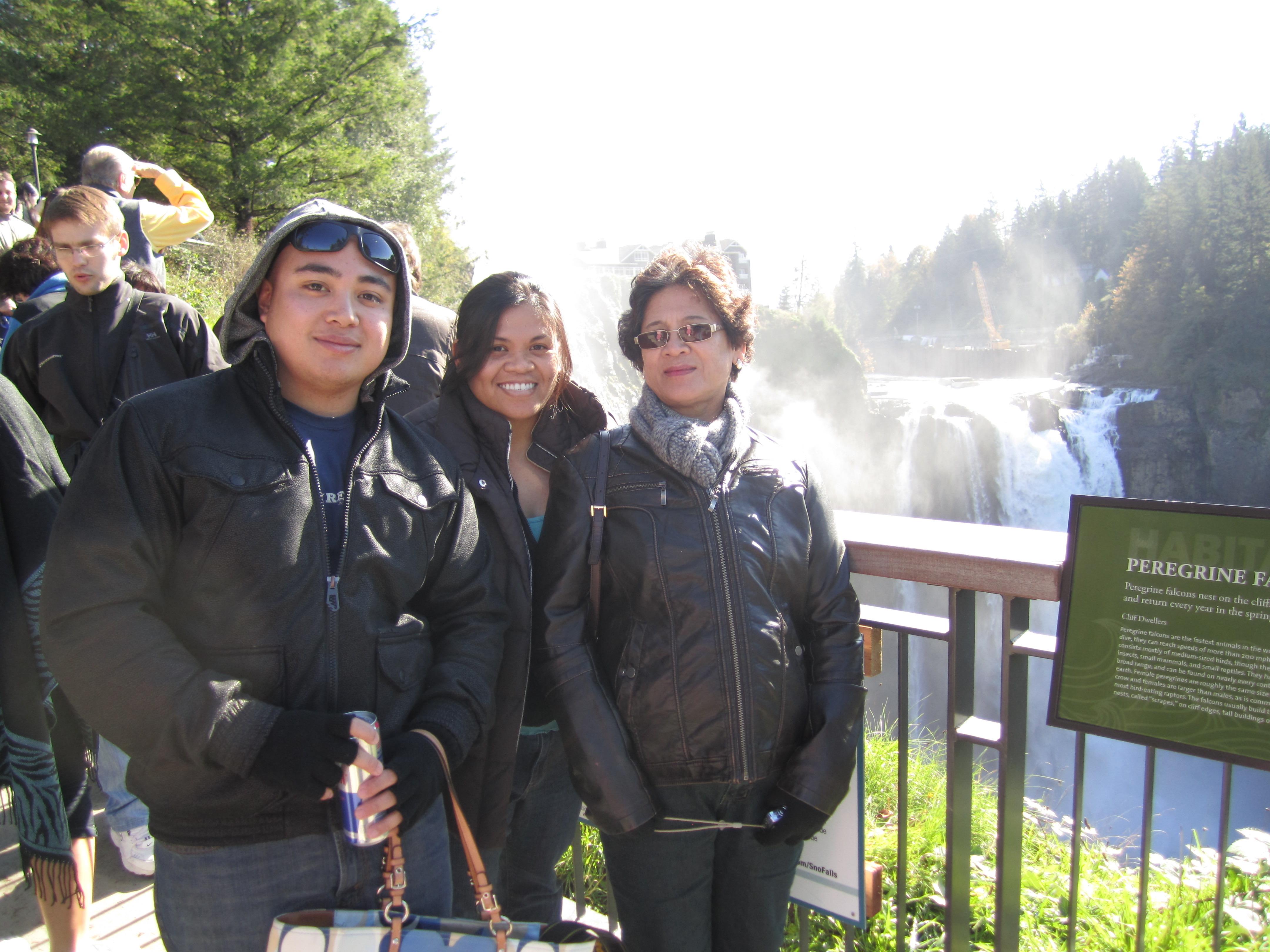 Three friends pose together with smiles, surrounded by nature near a stunning waterfall.