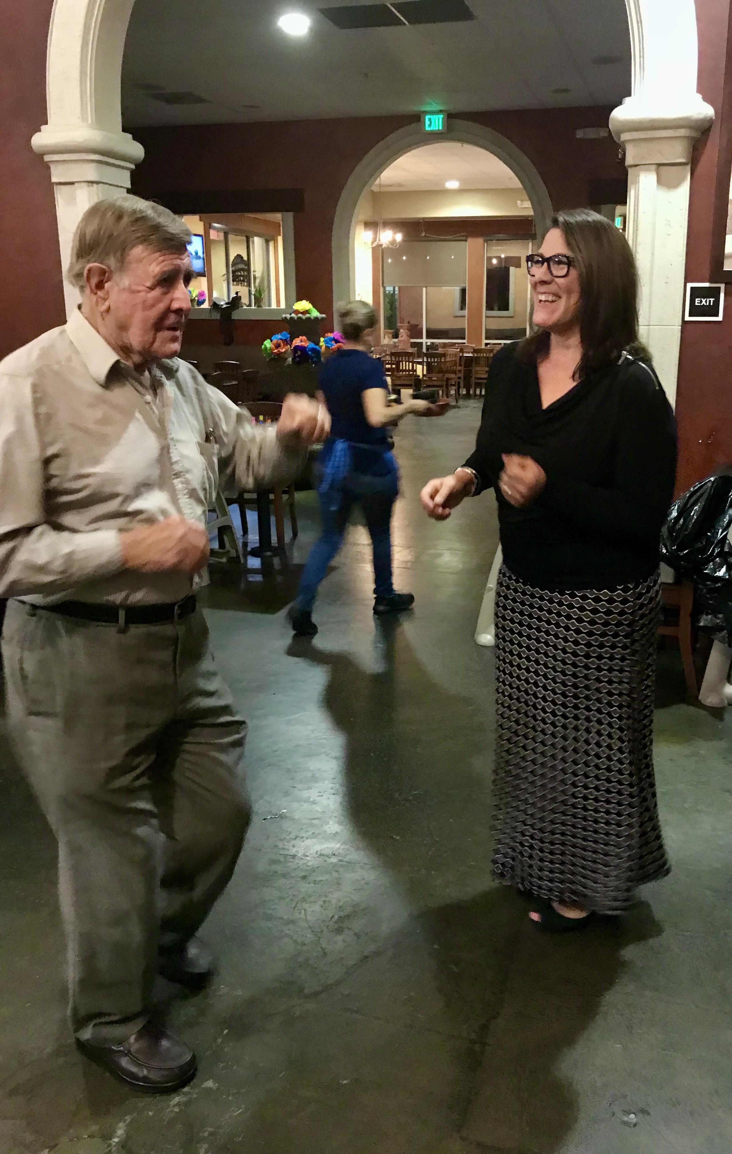 Two people are dancing happily together in a restaurant during a vibrant evening event.
